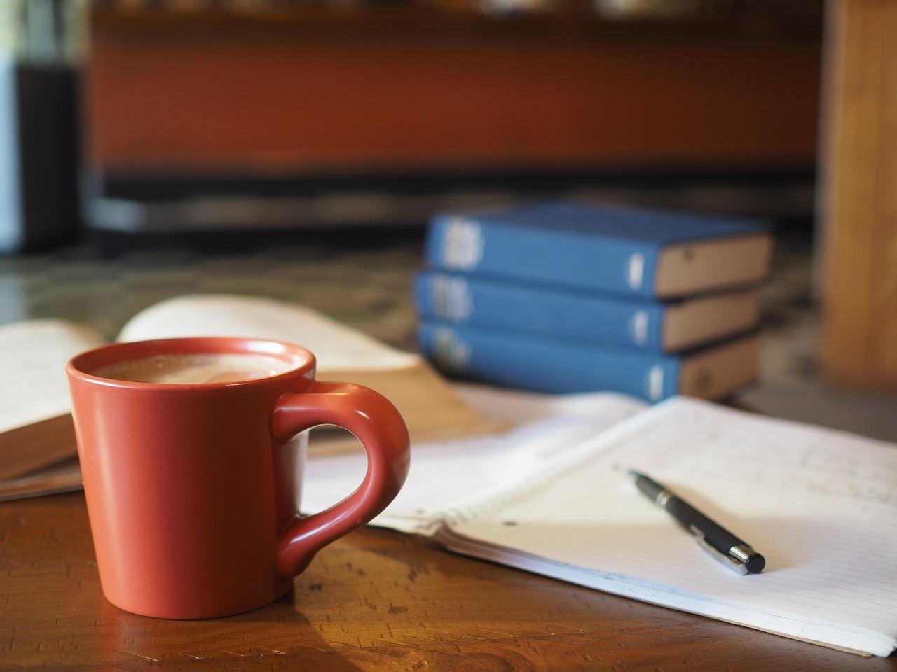 A steaming cup of coffee sits on a wooden desk beside an open notebook and colorful pens, inviting focus and productivity.
