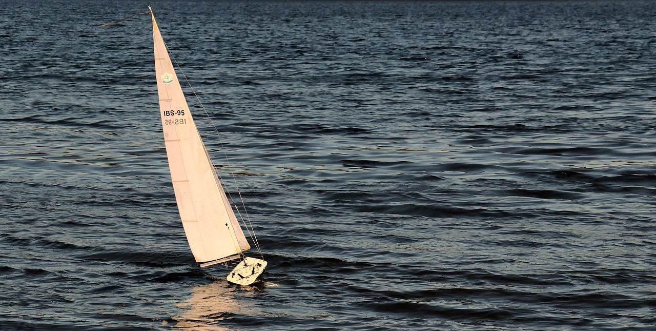A sleek RC sailboat glides across a shimmering lake, its colorful sails catching the gentle breeze.