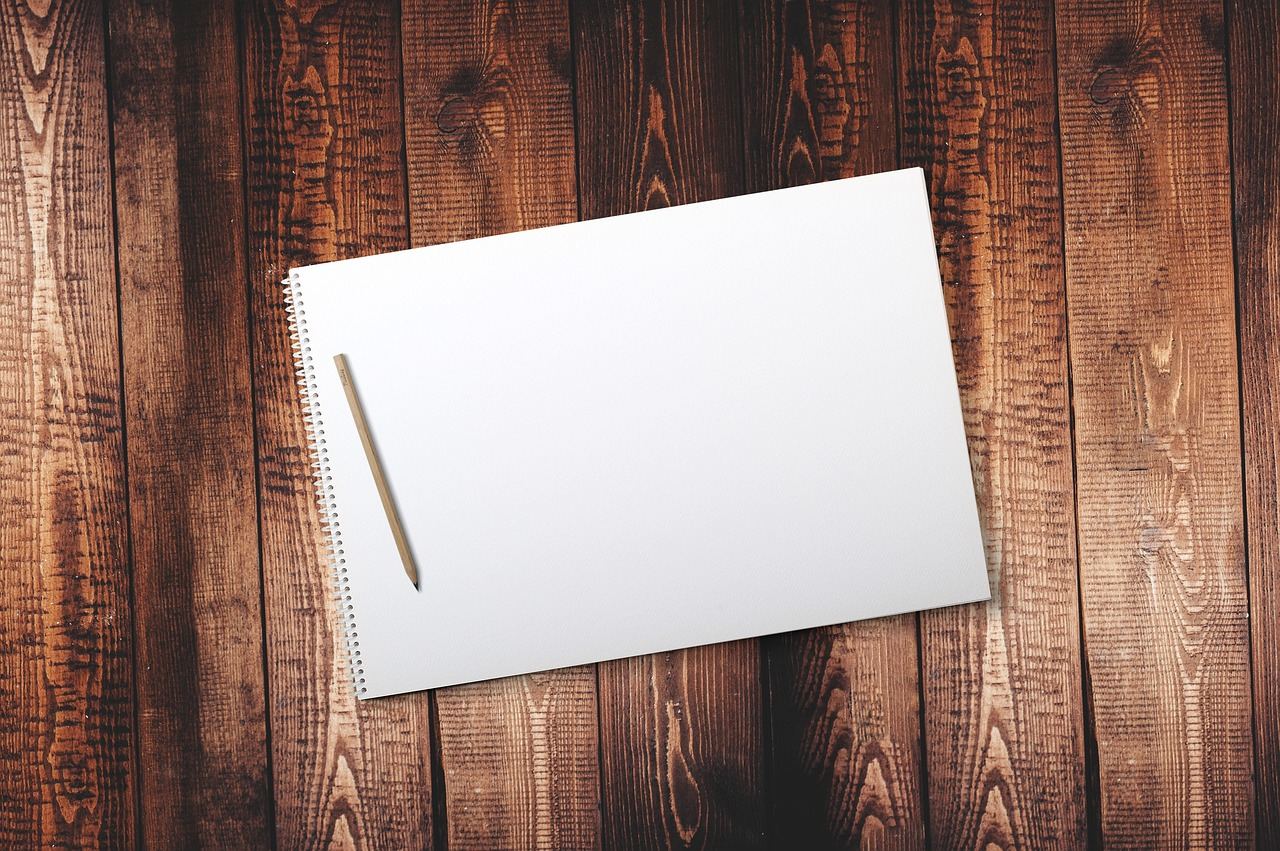 A close-up of a sketchbook open to a blank page, surrounded by colorful pencils and erasers.