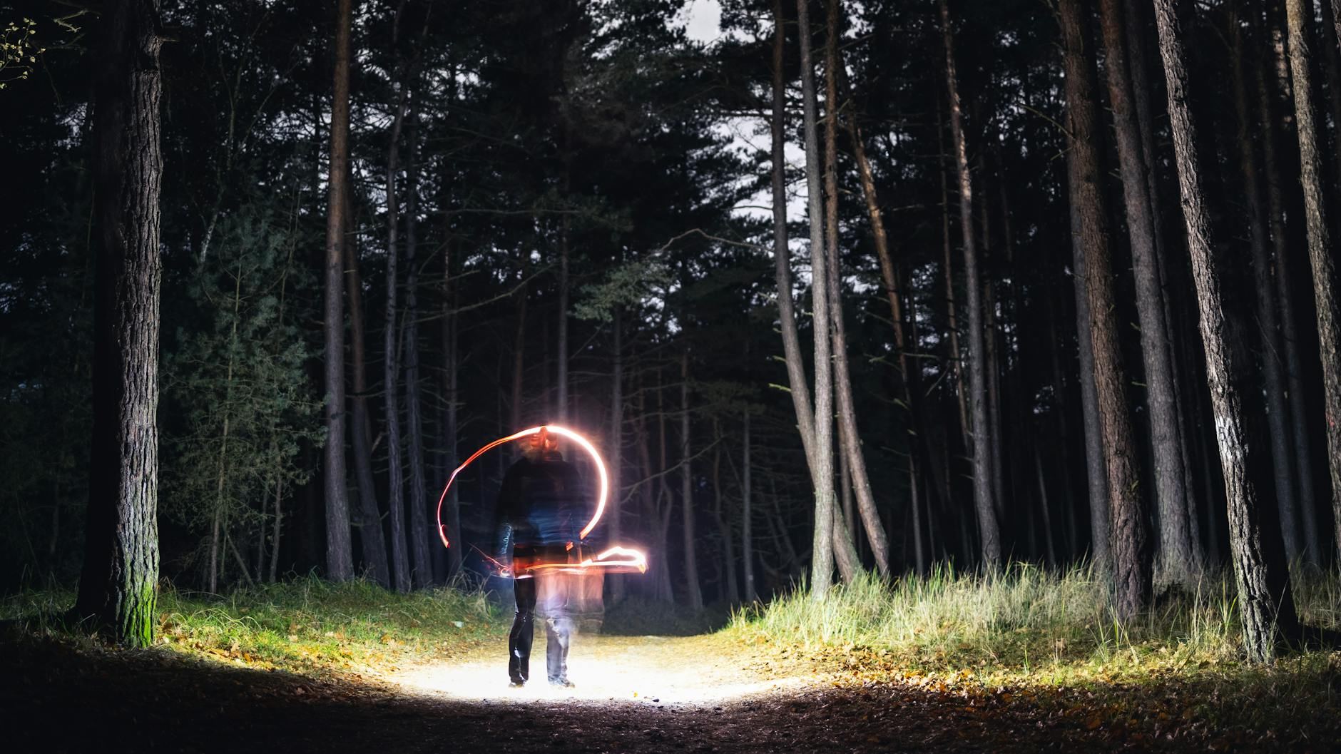 A mysterious figure creates light trails in a dark forest at night, evoking magic and mystery.