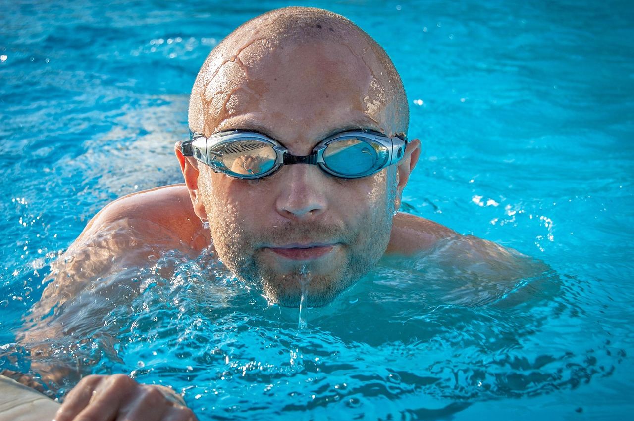 A focused male swimmer dives into a clear blue pool, creating splashes as he begins his race.