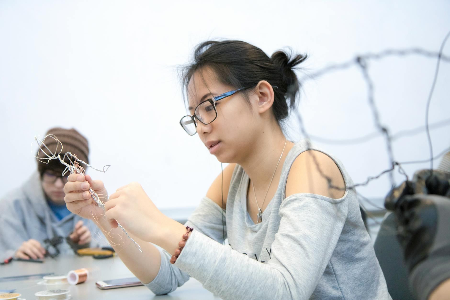 Focused young woman working on intricate wire sculpture in a creative workshop. Artistic expression and skill.