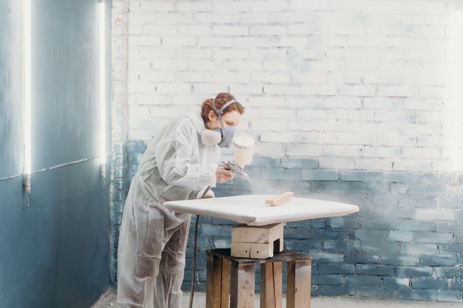 A woman in protective gear spray painting a wooden surface, showcasing techniques for mastering spray paint art.