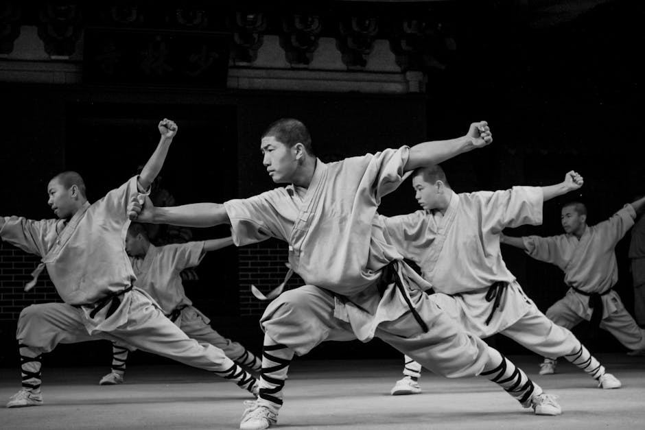 Five martial artists demonstrate synchronized Shaolin Kung Fu poses in traditional attire.