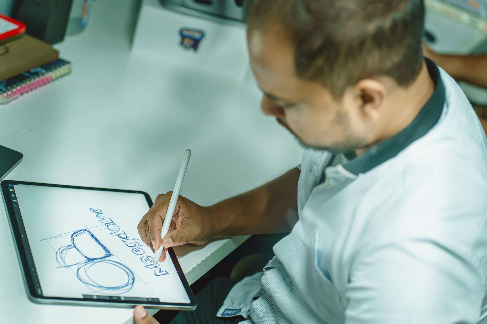An adult man sketching on a digital tablet, focusing on design work in an office environment.