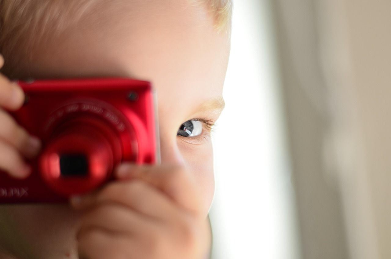 A child playfully holding a camera, exploring portrait photography in a bright, inviting setting.