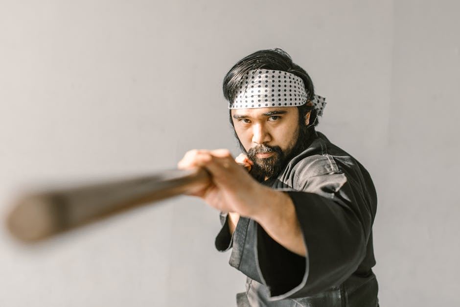A martial artist in a black gi practices Aikido with a wooden staff, showcasing focus and technique.