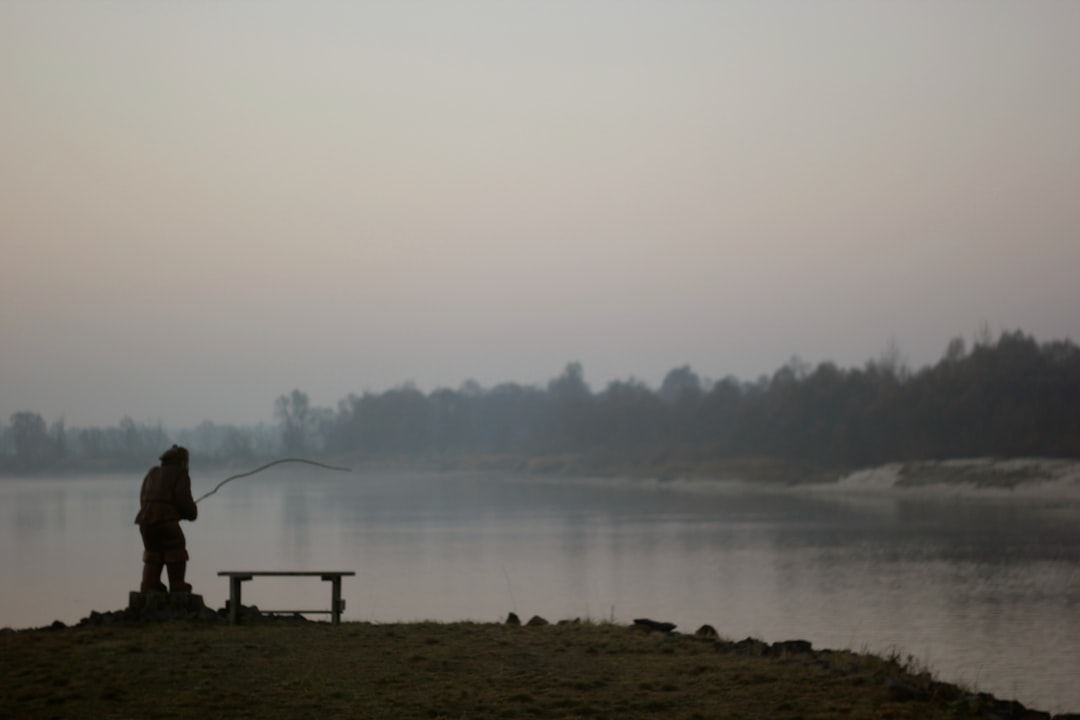 A lone fisherman casts a line by a misty lake.