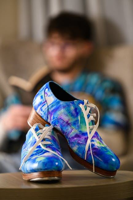 A pair of colorful tap dance shoes with a blurred figure in the background, suggesting a dance context.