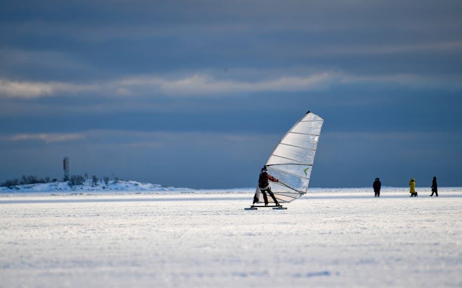 A person ice sailing on a frozen lake with others in the background, showcasing the sport.