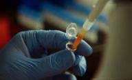 Anthropic's official close-up photograph of a gloved scientist pipetting a laboratory sample for the Claude enzyme discovery report