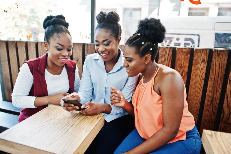 Three friends at a café table looking at one phone together
