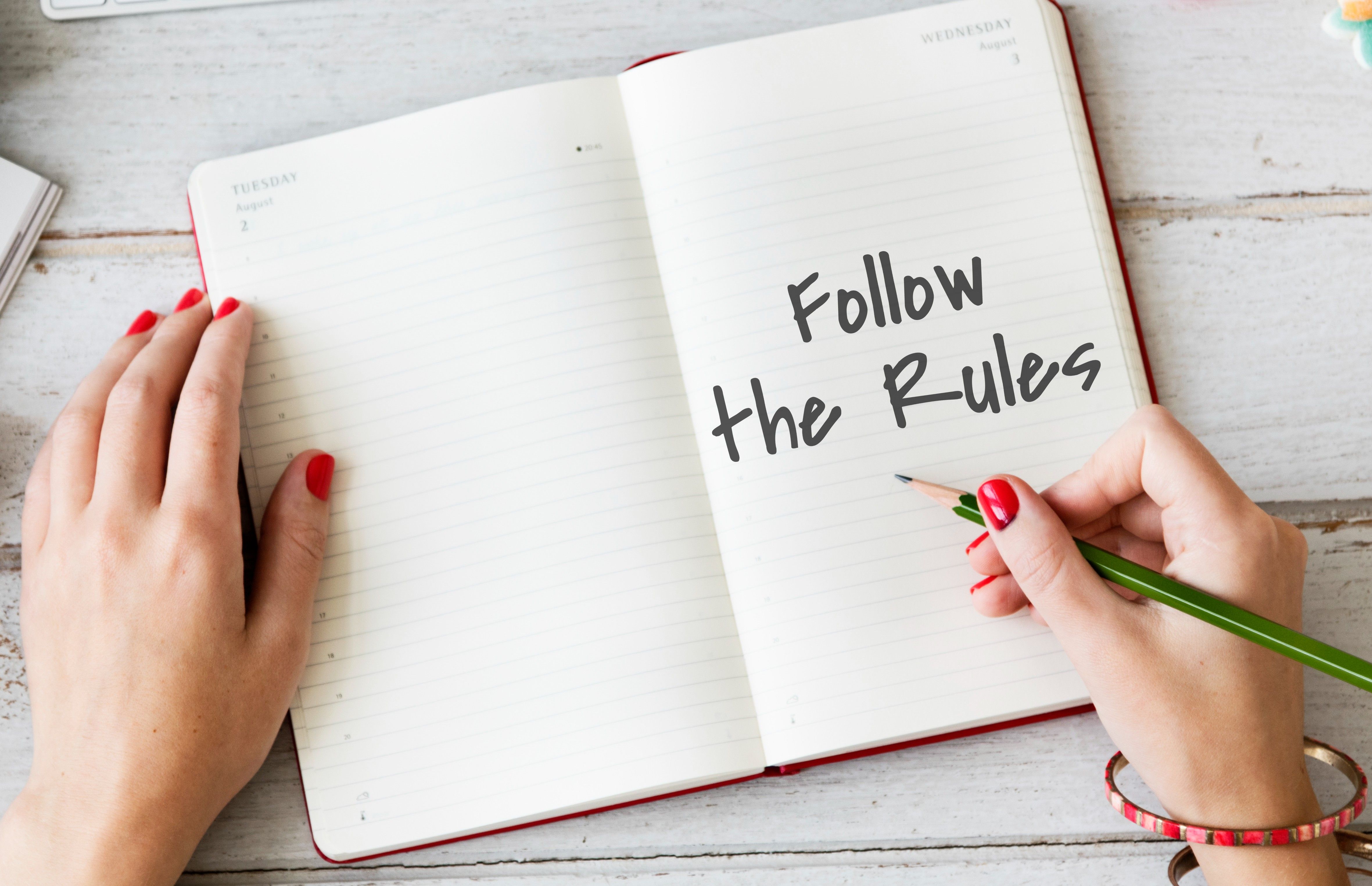 A hand writing "Follow the Rules" in an open notebook, symbolizing the unspoken etiquette of borrowing.