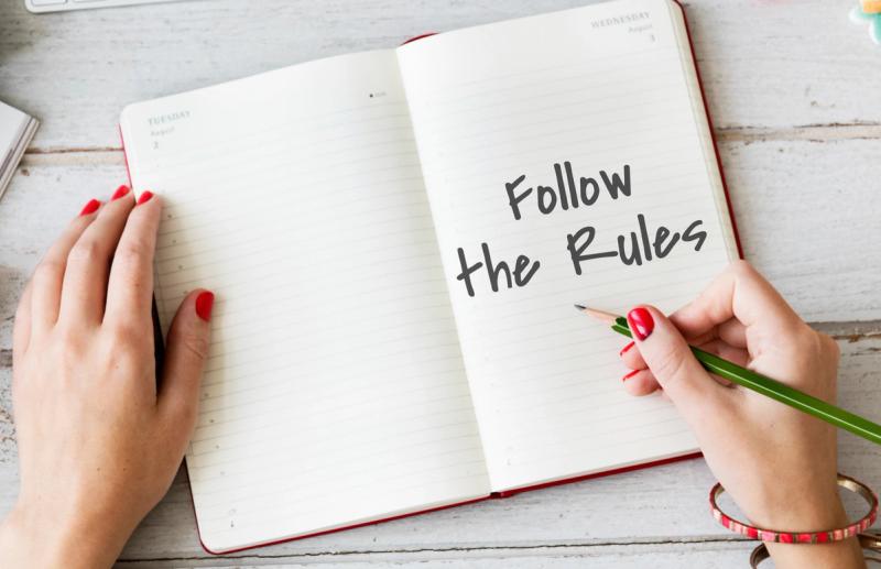 A hand writing "Follow the Rules" in an open notebook, symbolizing the unspoken etiquette of borrowing.