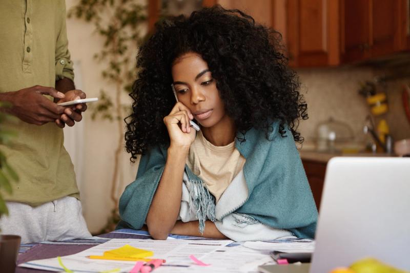 A woman at her kitchen table with bills and a laptop, on the phone