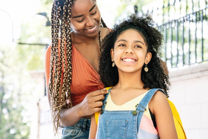 A mother seeing her daughter off to school with a backpack