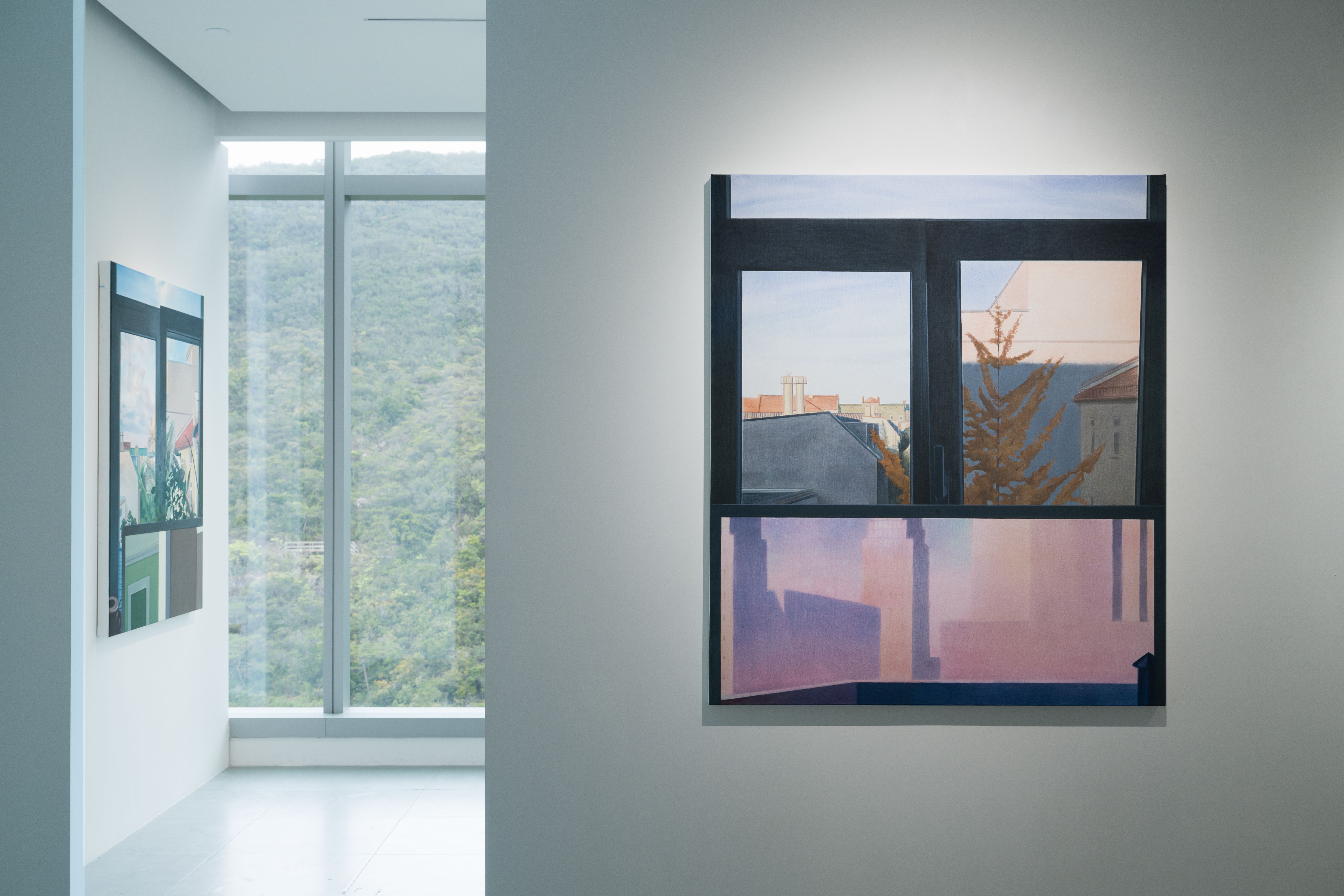 An installation shot of an art gallery with two paintings and a view onto a wooded area
