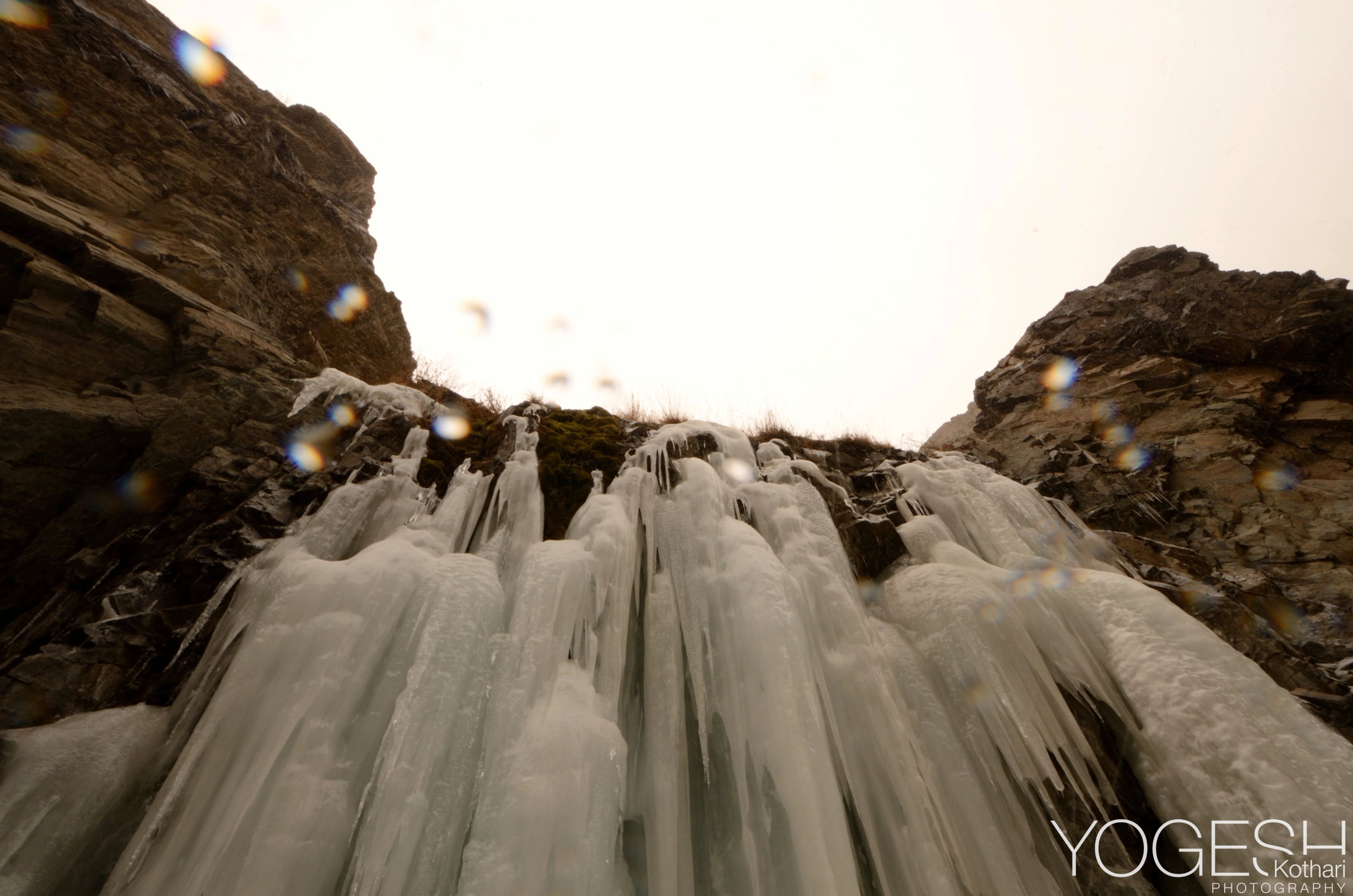 Frozen waterfall of hanging icicles seen from below against a pale sky
