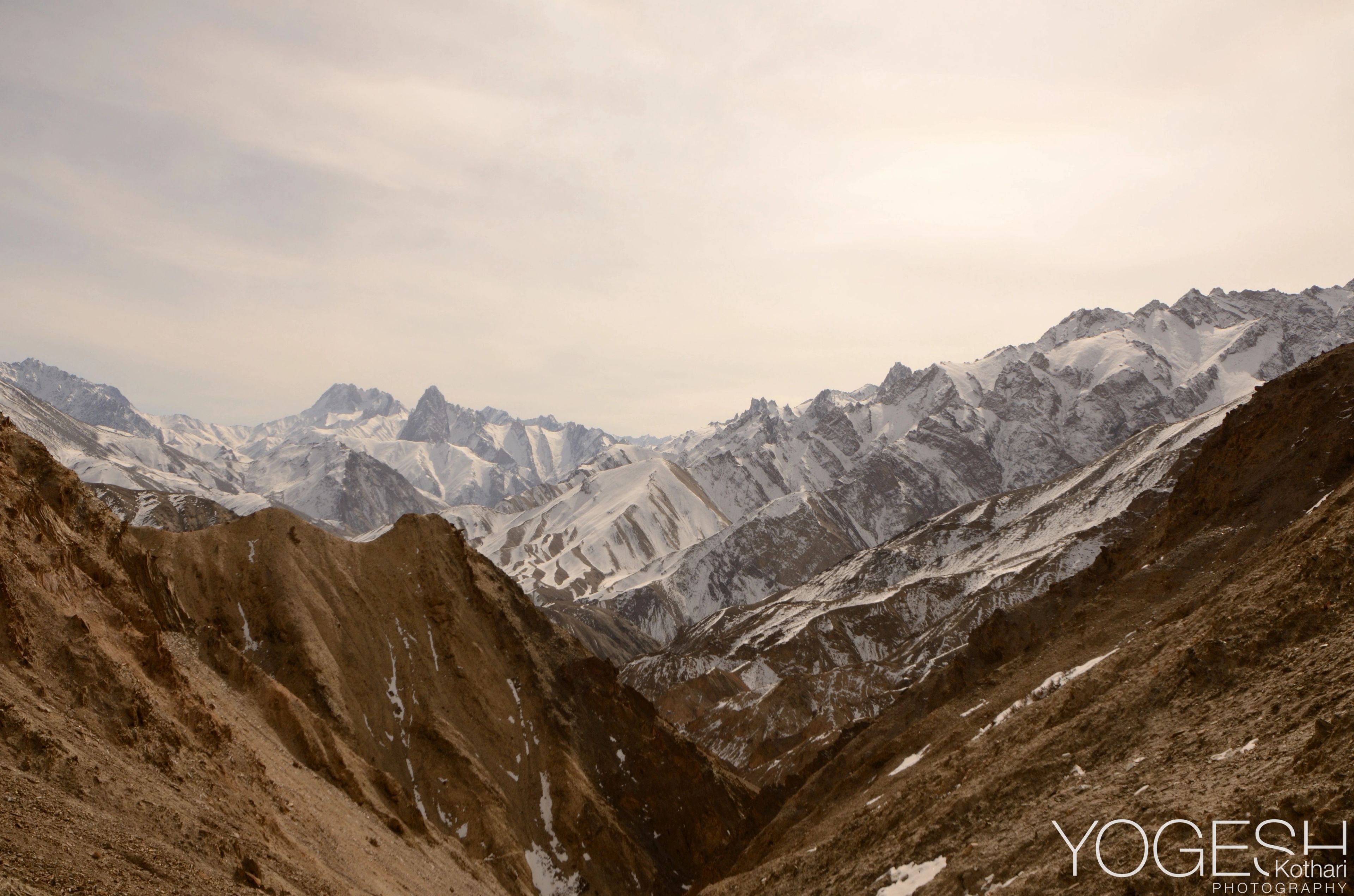 Brown valley slopes leading to a range of snow-covered peaks