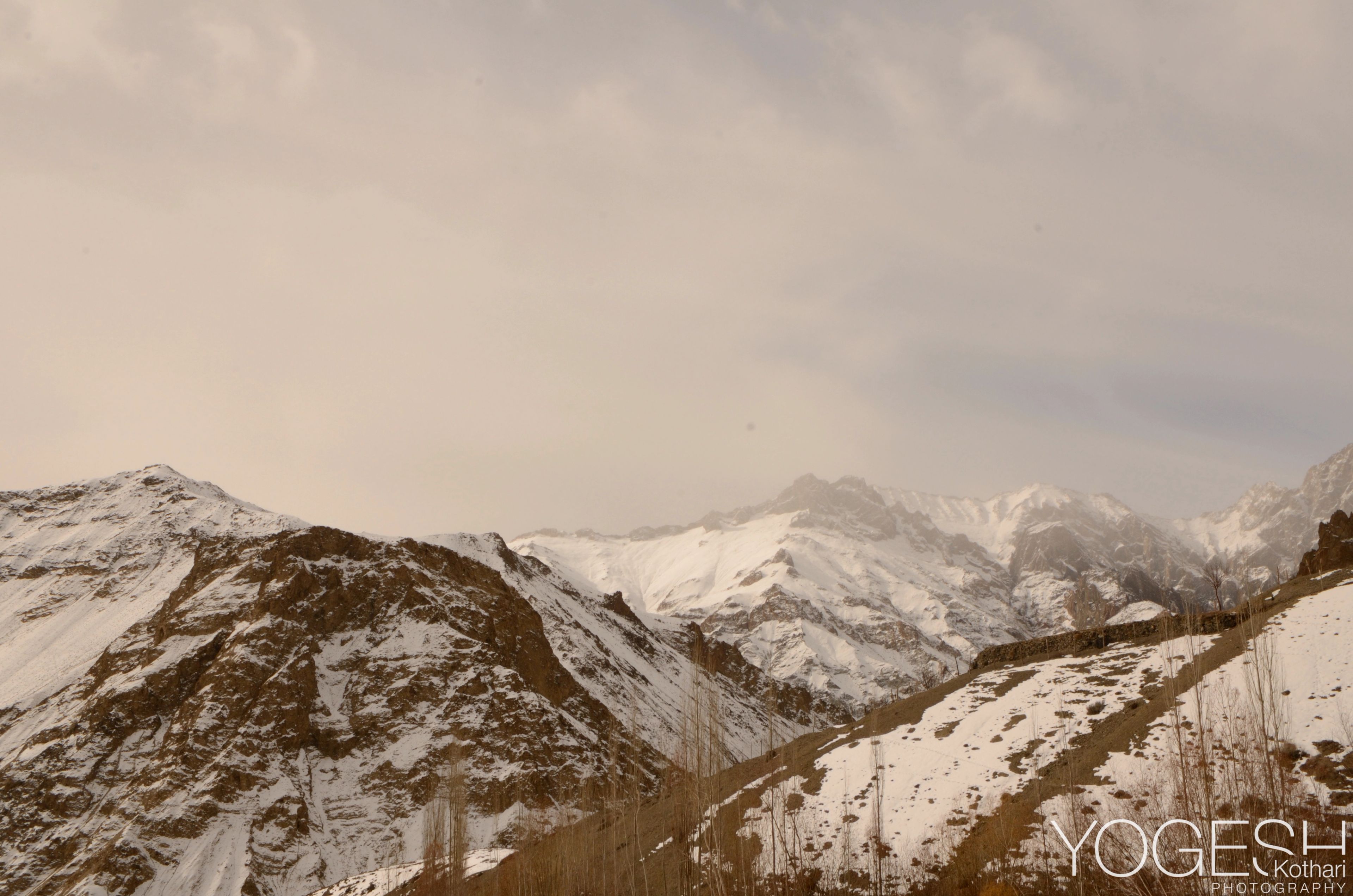 Snow-covered valley slopes under a hazy sky, distant peaks fading into mist