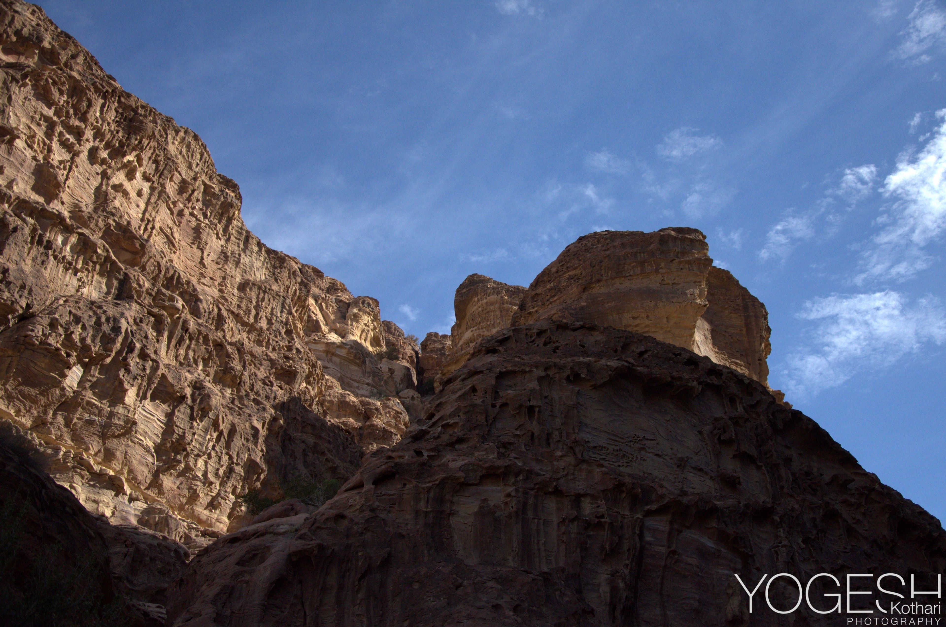 Steep sandstone cliffs and rock peaks rising into a blue sky with light cloud