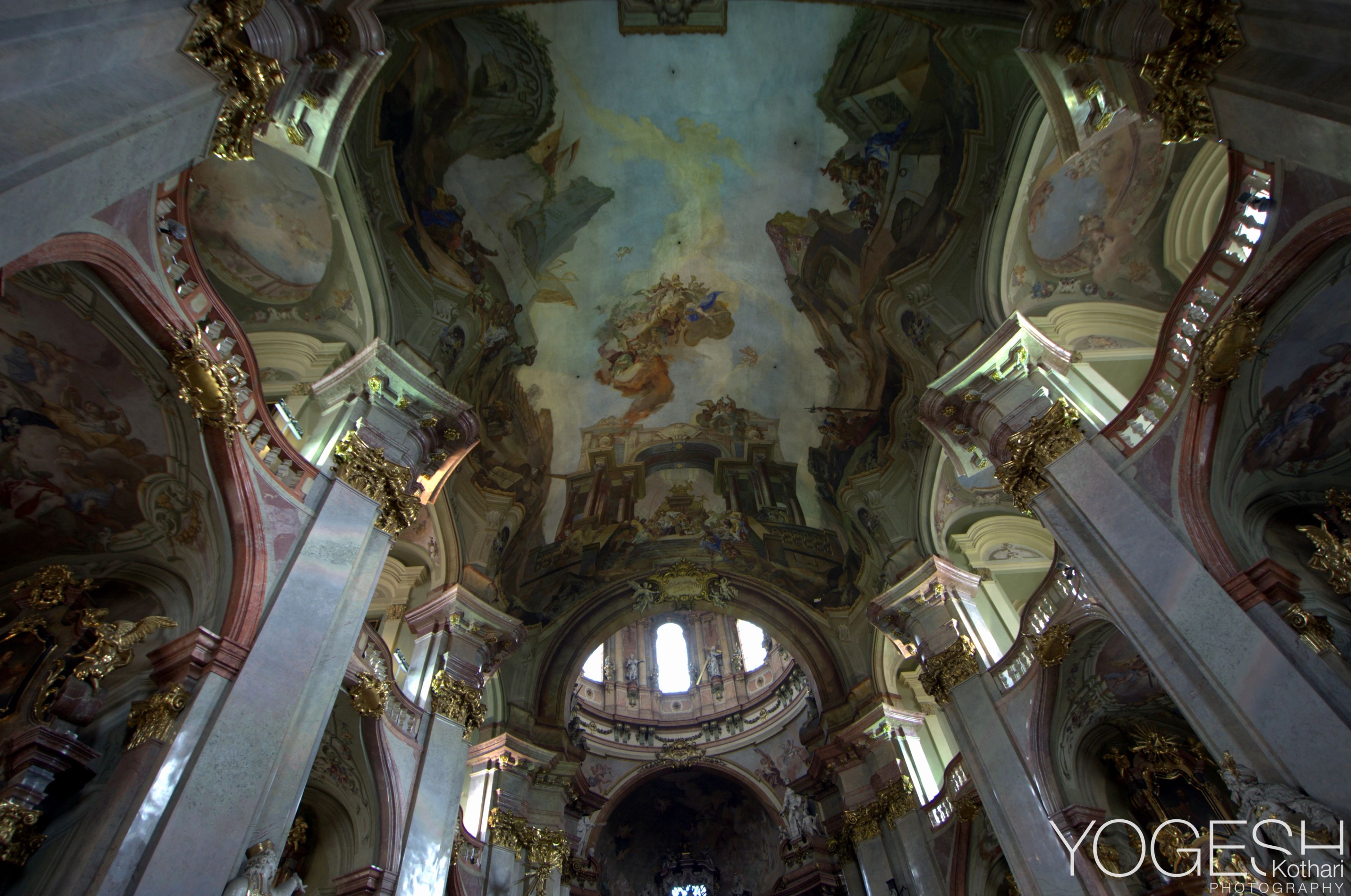Ornate Baroque church interior, looking up at painted ceiling frescoes and a dome