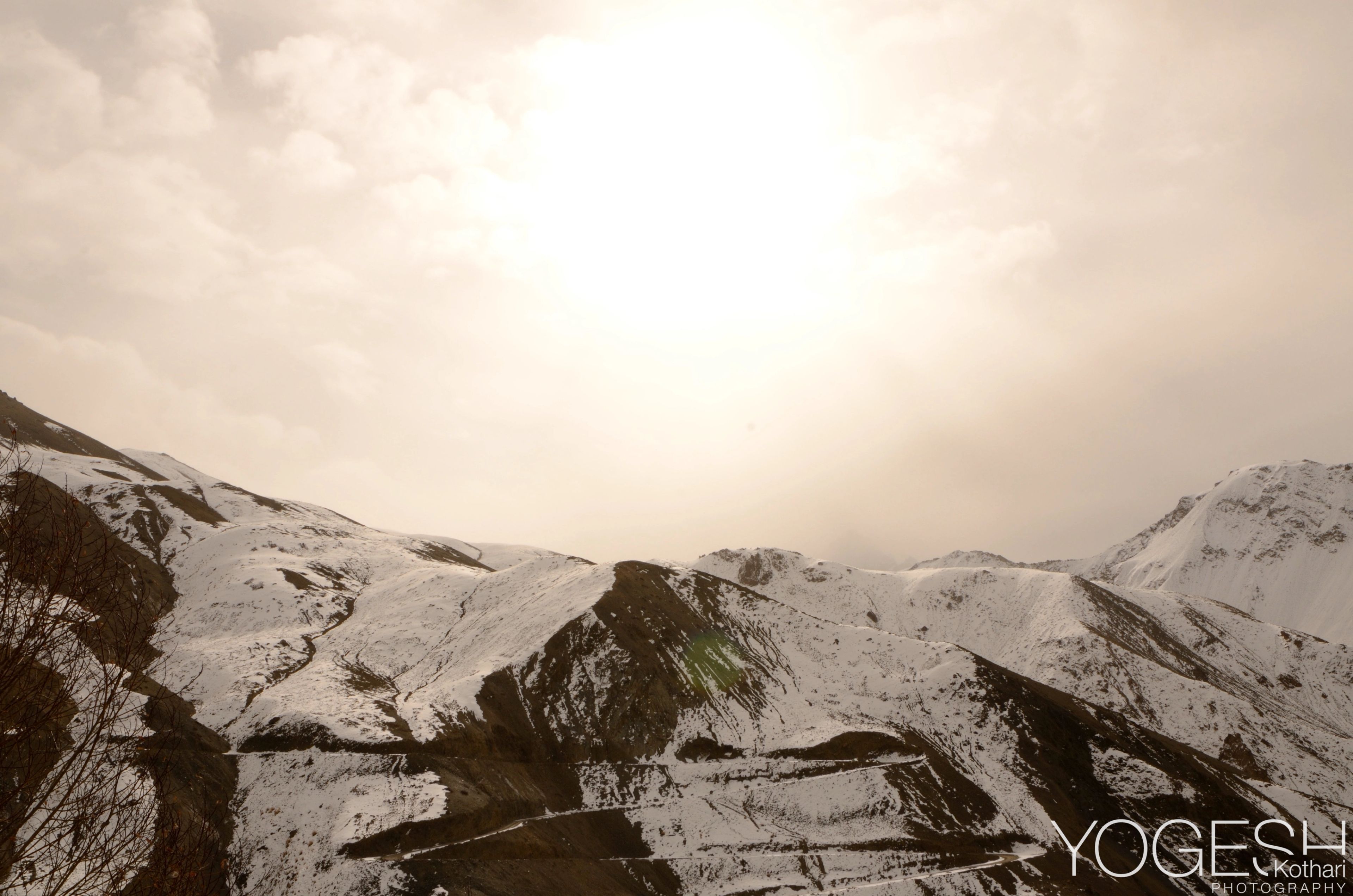 Snow-streaked mountain ridges under a bright, hazy sun