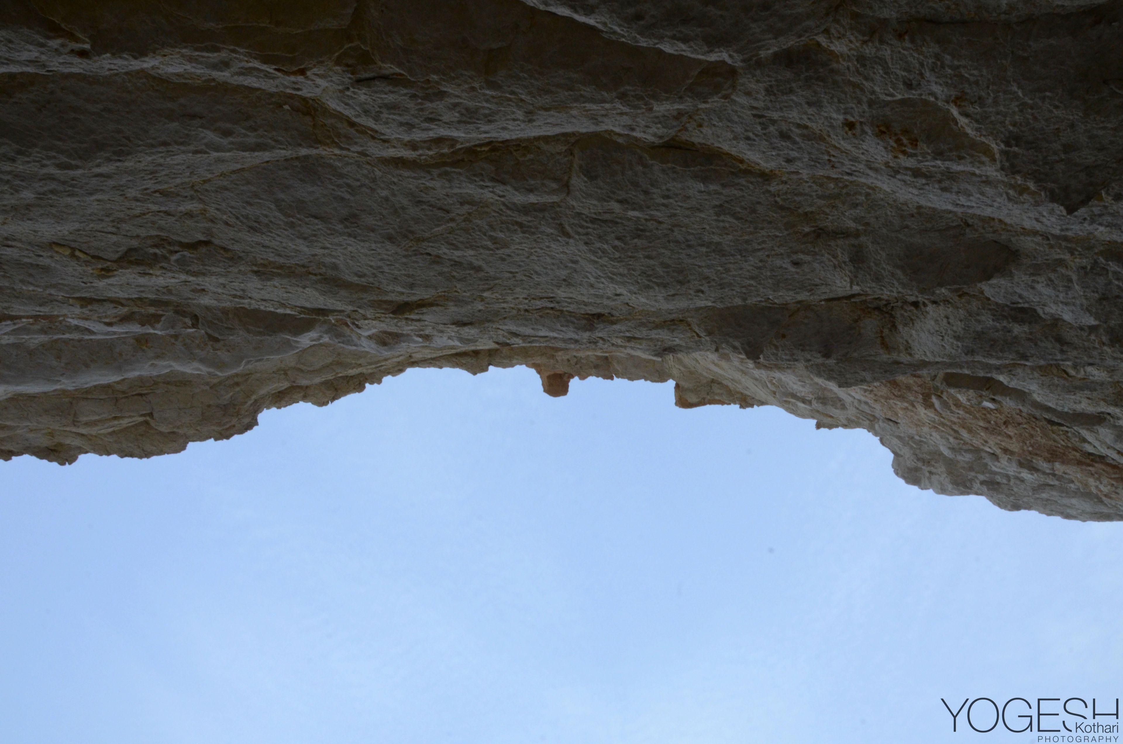 Blue sky seen from beneath the overhanging roof of a rock cave