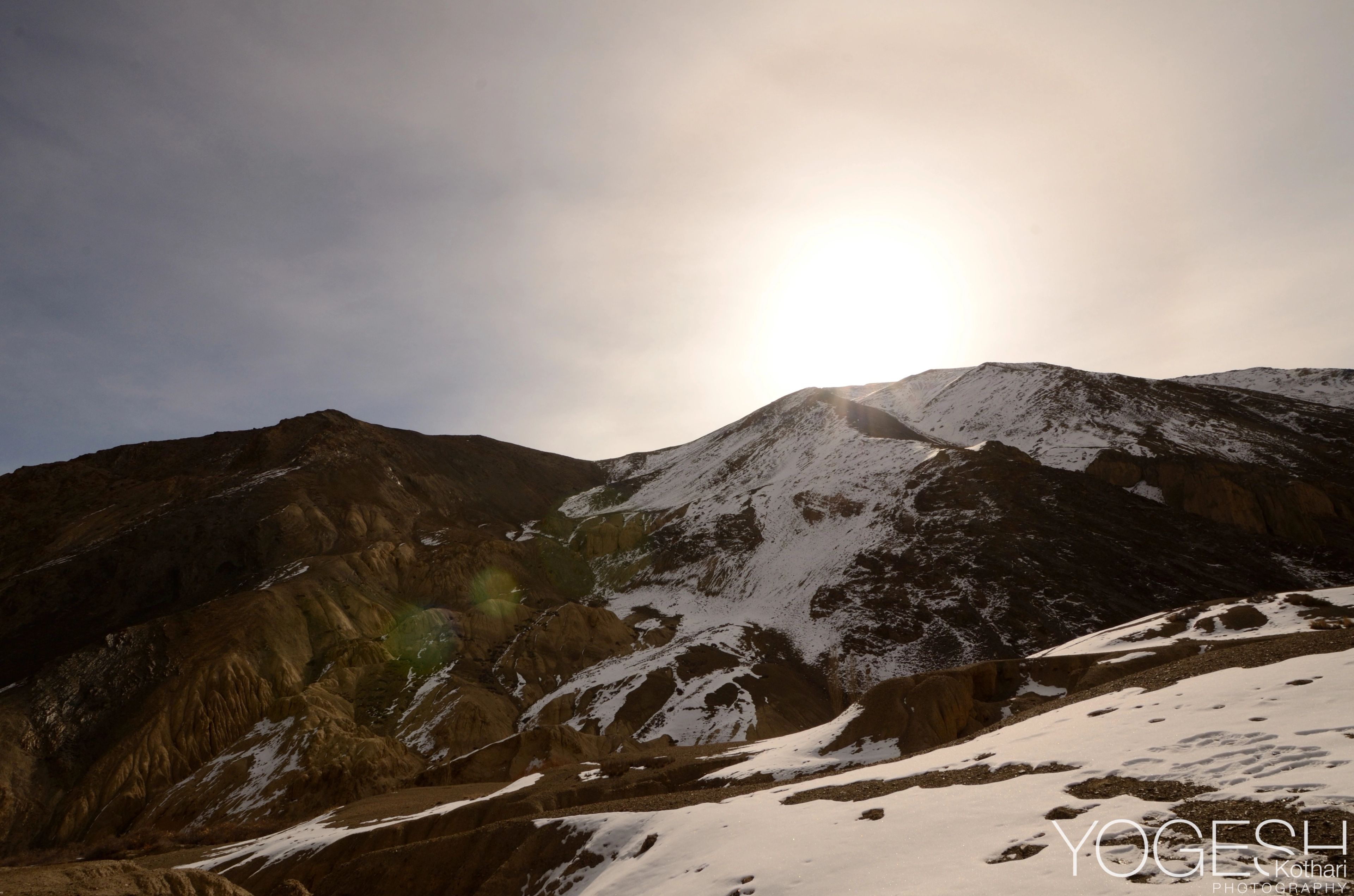 Sun glowing through haze above snow-patched mountain slopes
