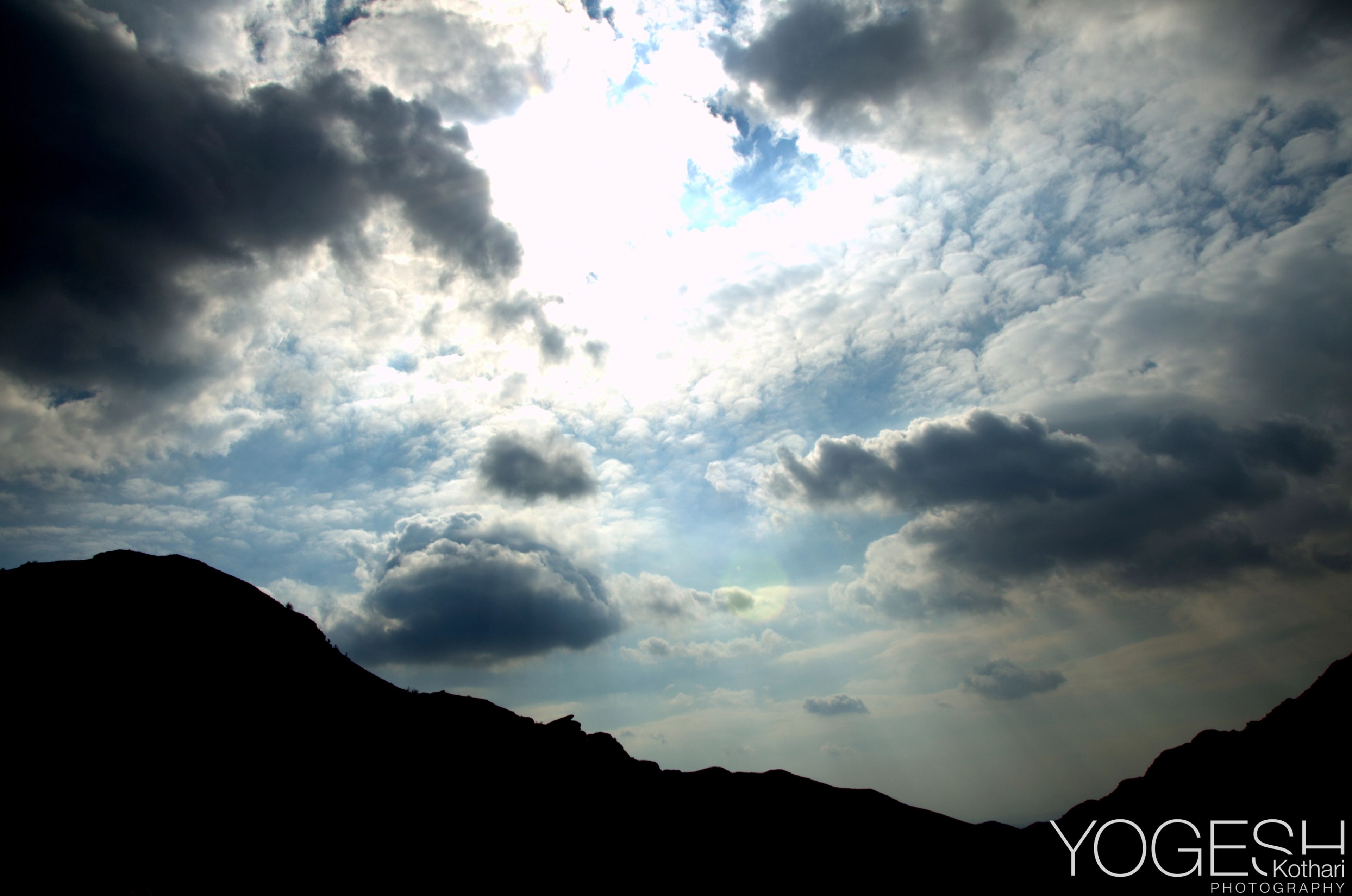 Sunlight breaking through scattered clouds above dark mountain silhouettes