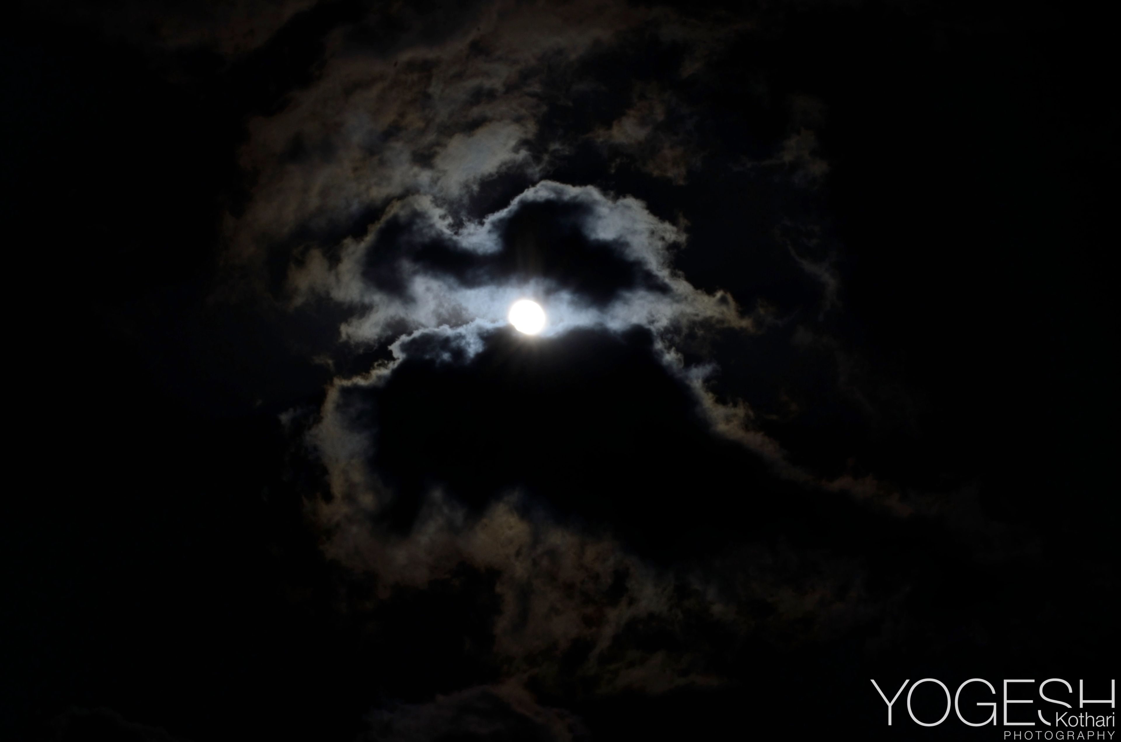 Full moon glowing through a gap in dark night clouds