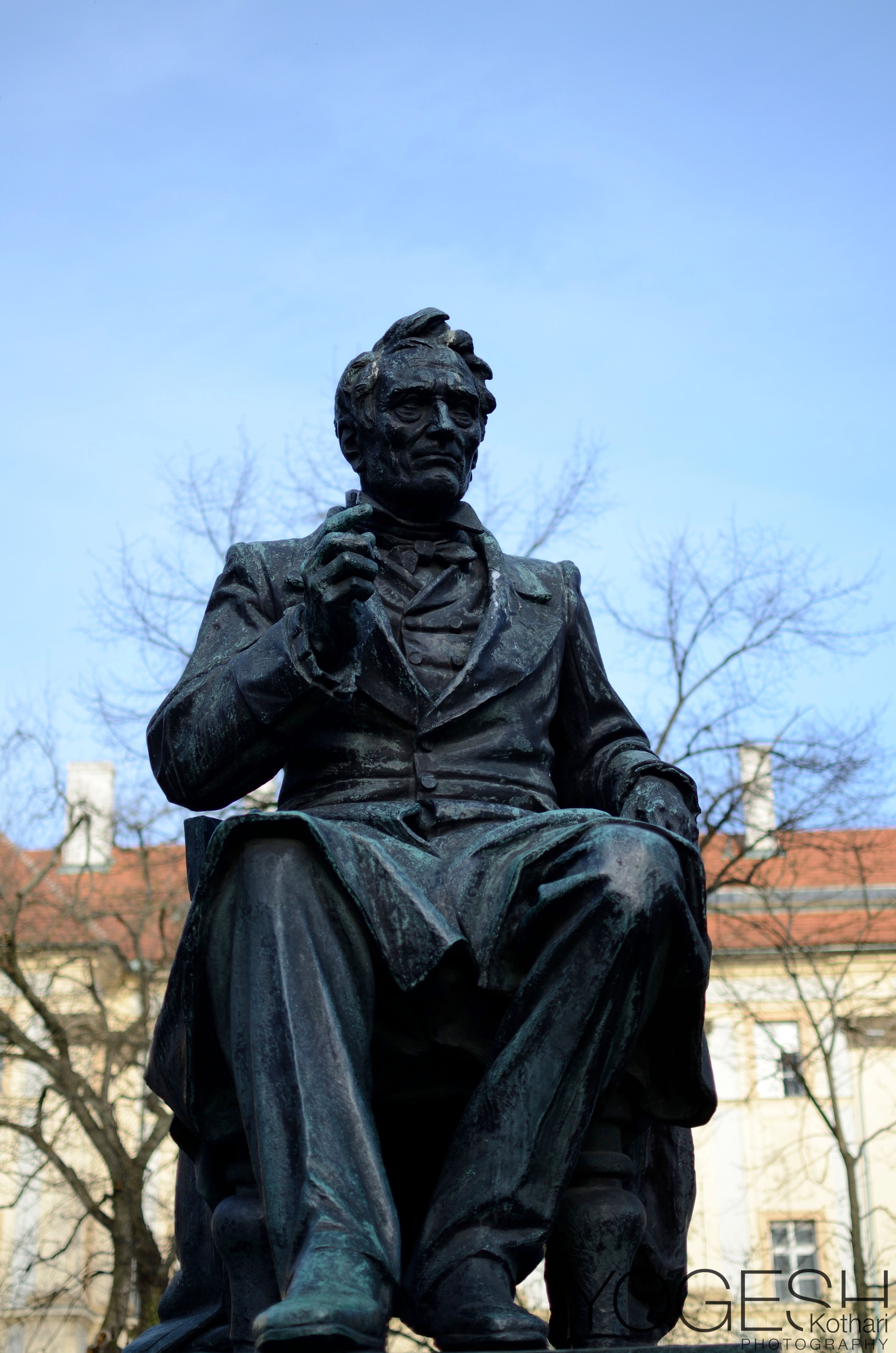 Bronze statue of a seated man in a frock coat against a blue sky