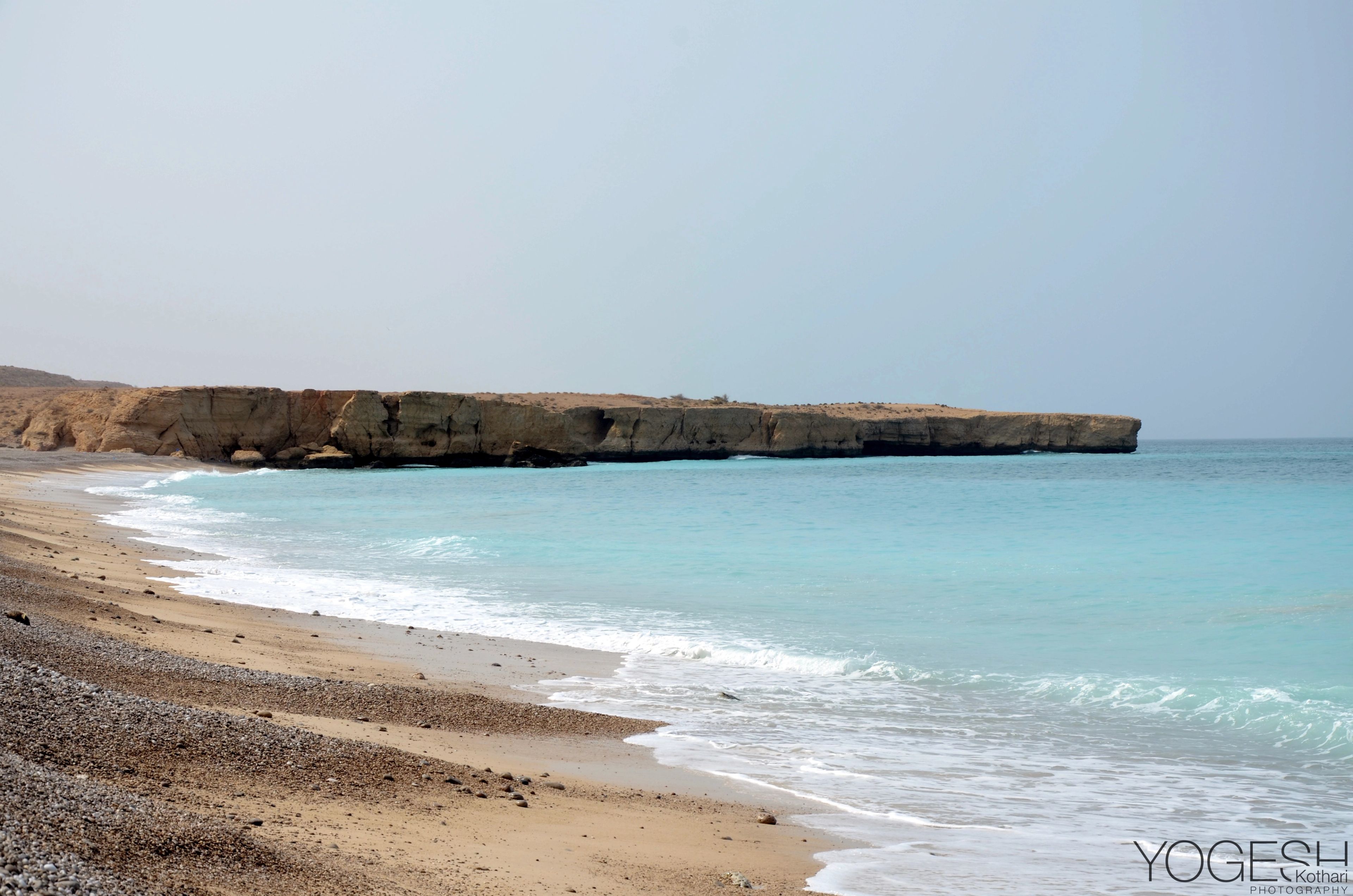 Curving beach and turquoise water below a long, flat-topped rocky headland