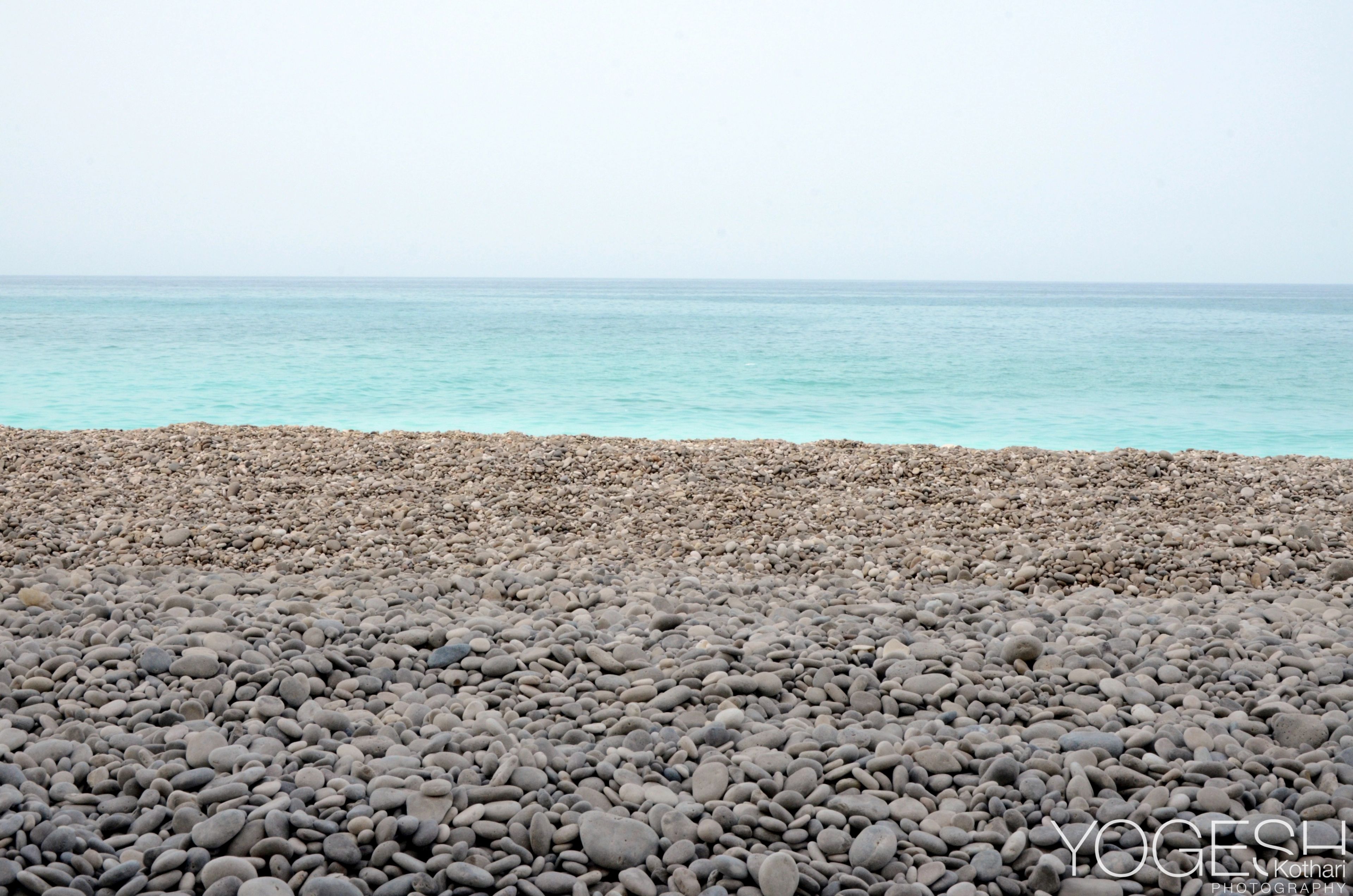 Beach of smooth grey pebbles stretching to a calm turquoise sea