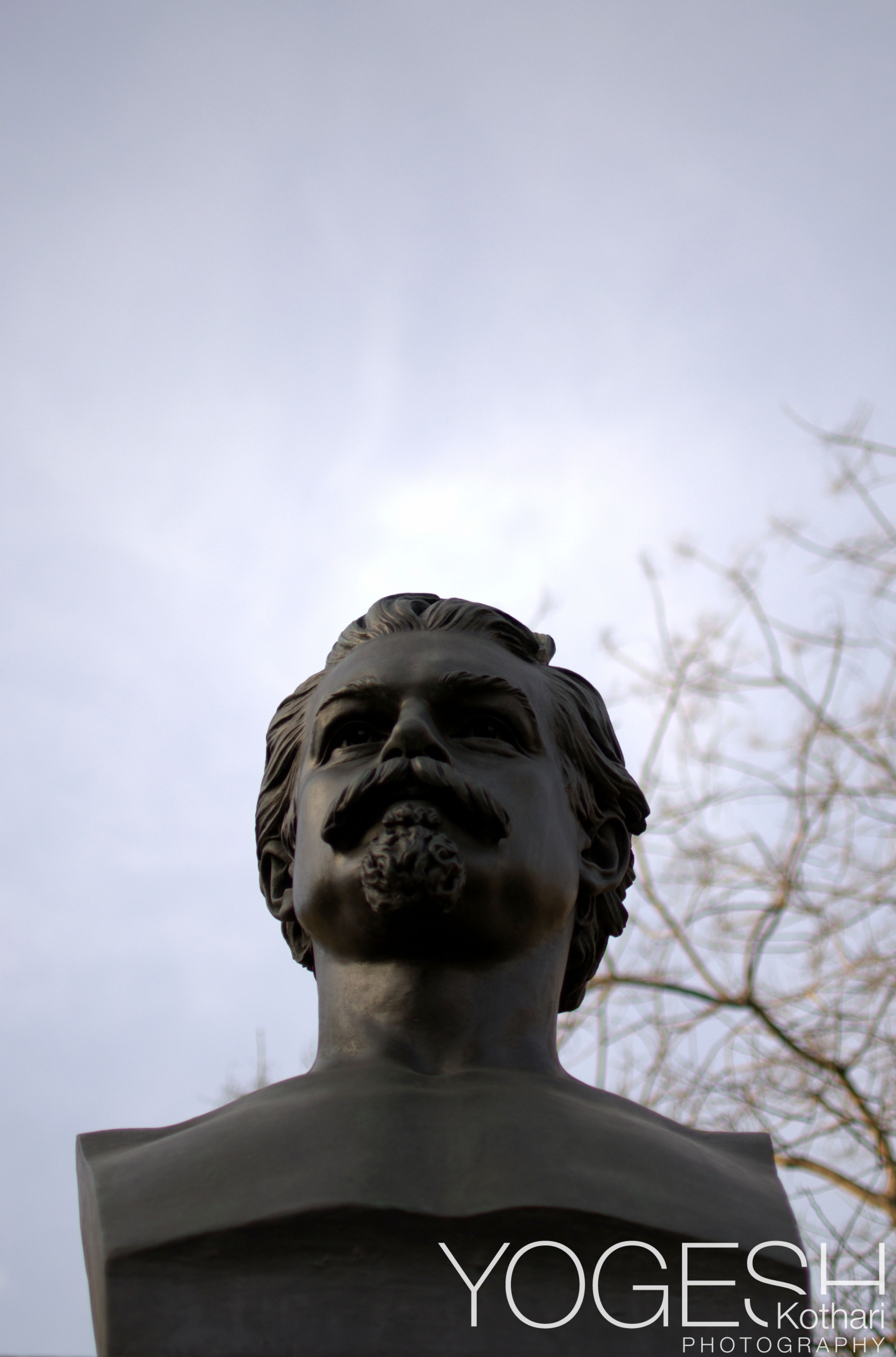 Bronze bust of a bearded man, seen from below against a pale sky