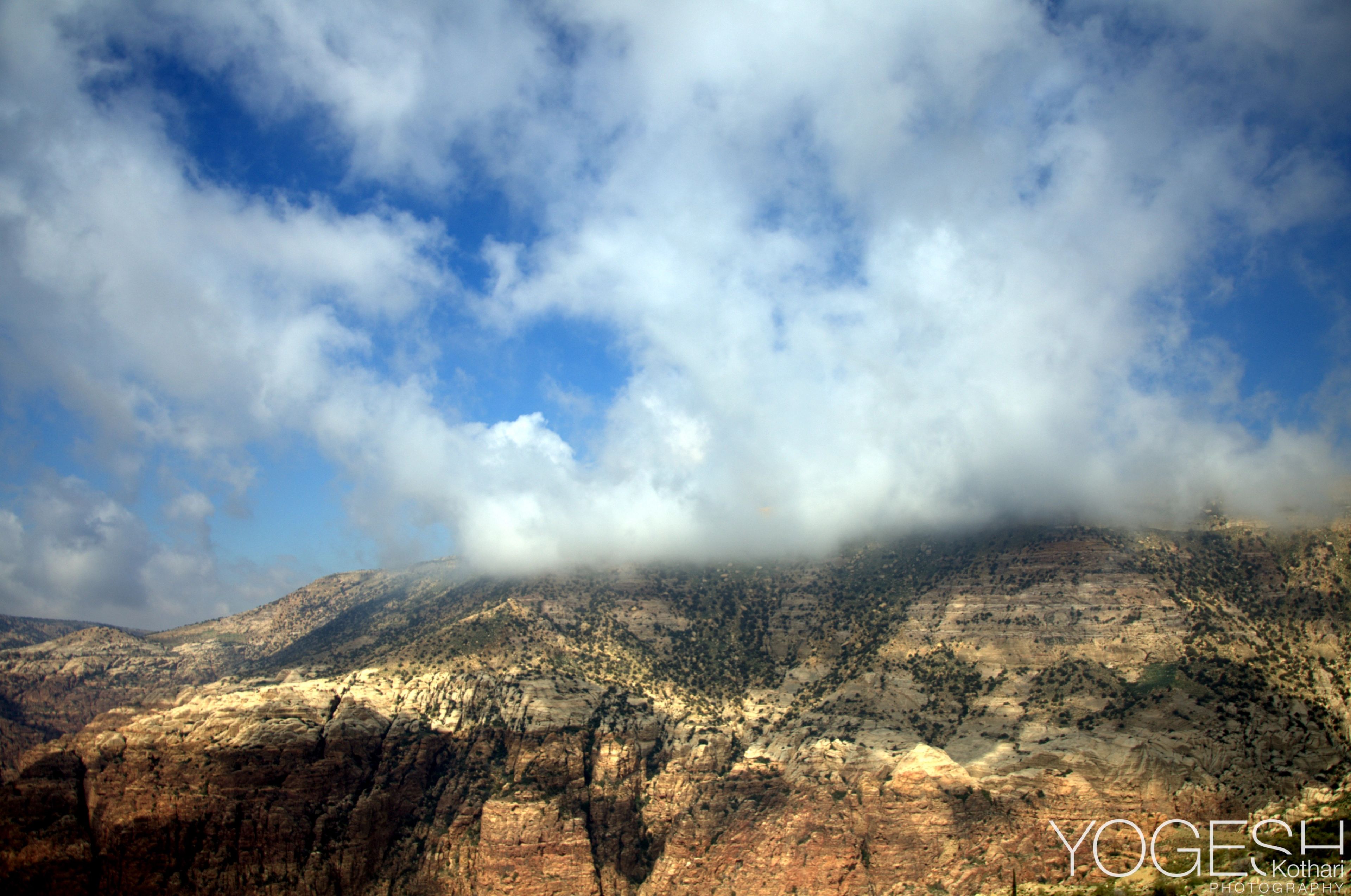 Clouds spilling over a rugged mountain ridge under a blue sky