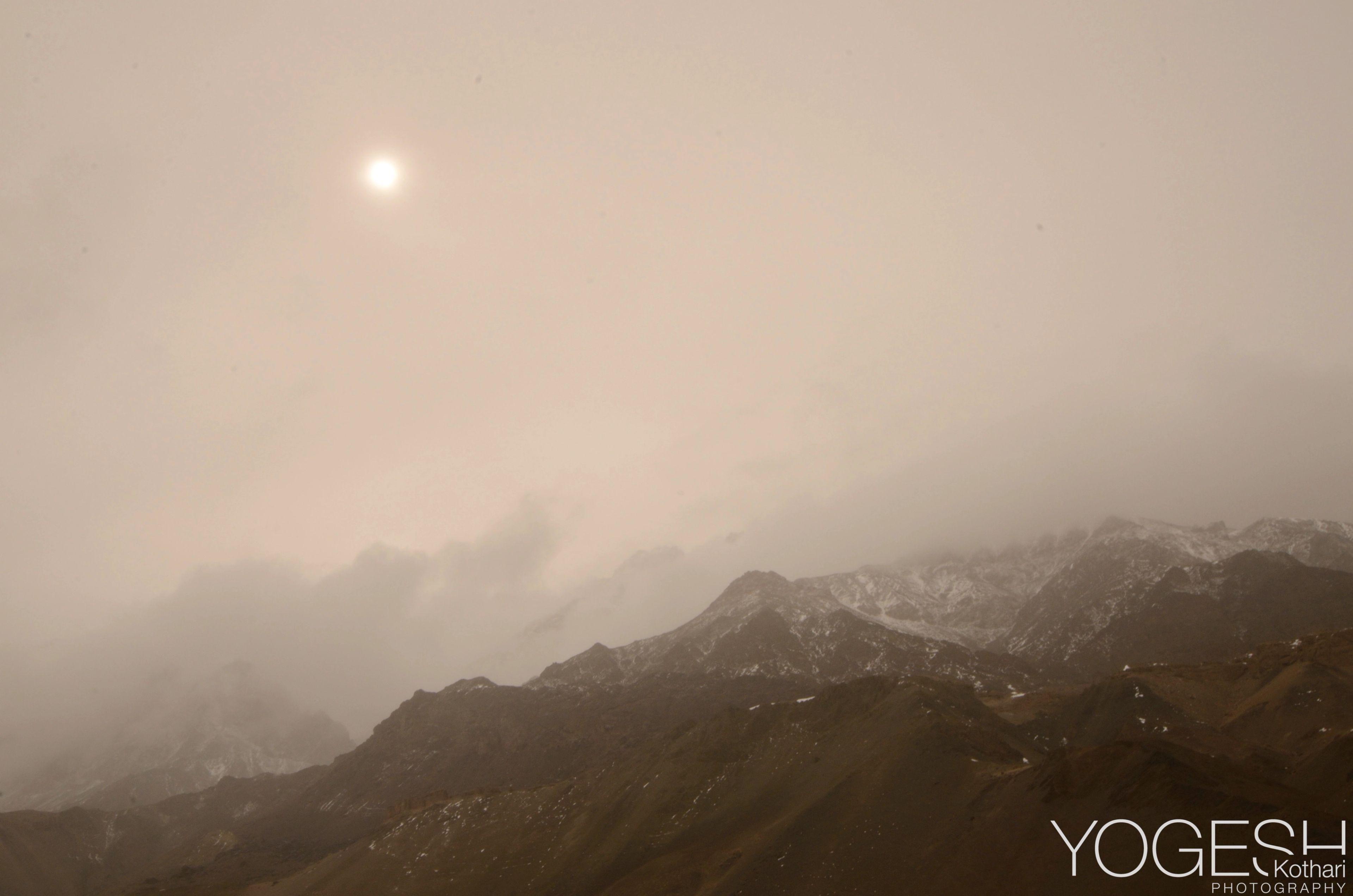 Mountain range softened by mist, a pale sun in a sepia sky