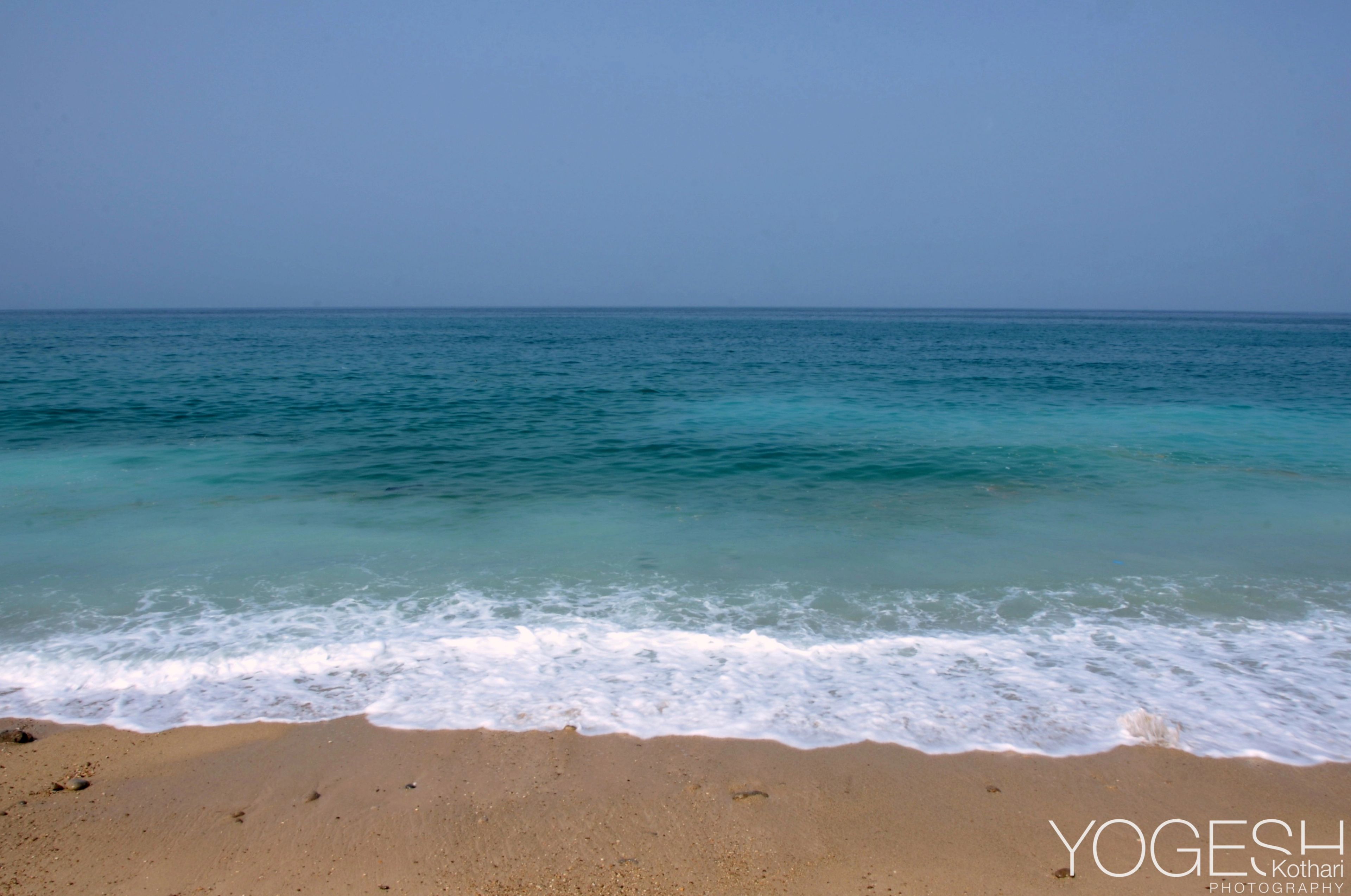 Turquoise sea meeting a sandy beach under a pale sky, a thin line of surf at the shore