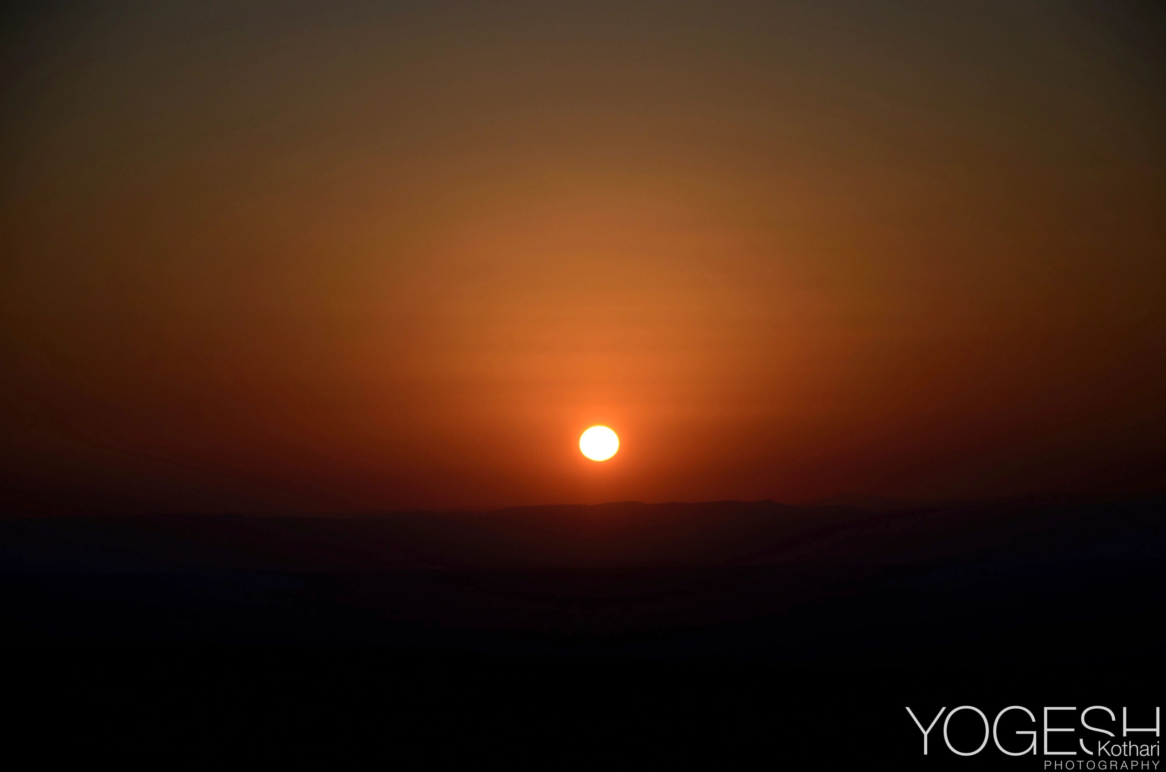 Red sun low over a dark horizon in an orange sky
