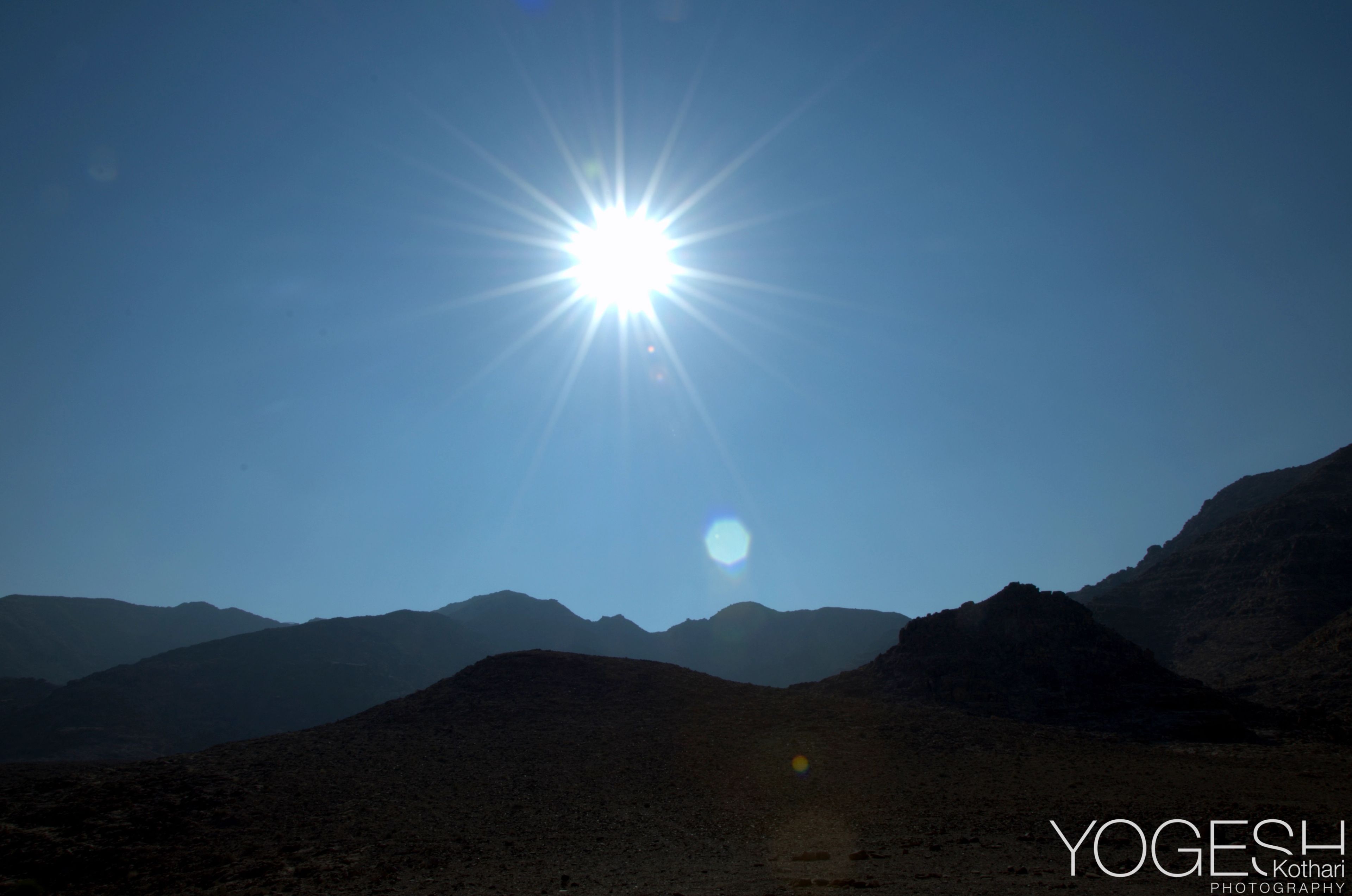 Bright sun with a starburst above silhouetted desert mountains