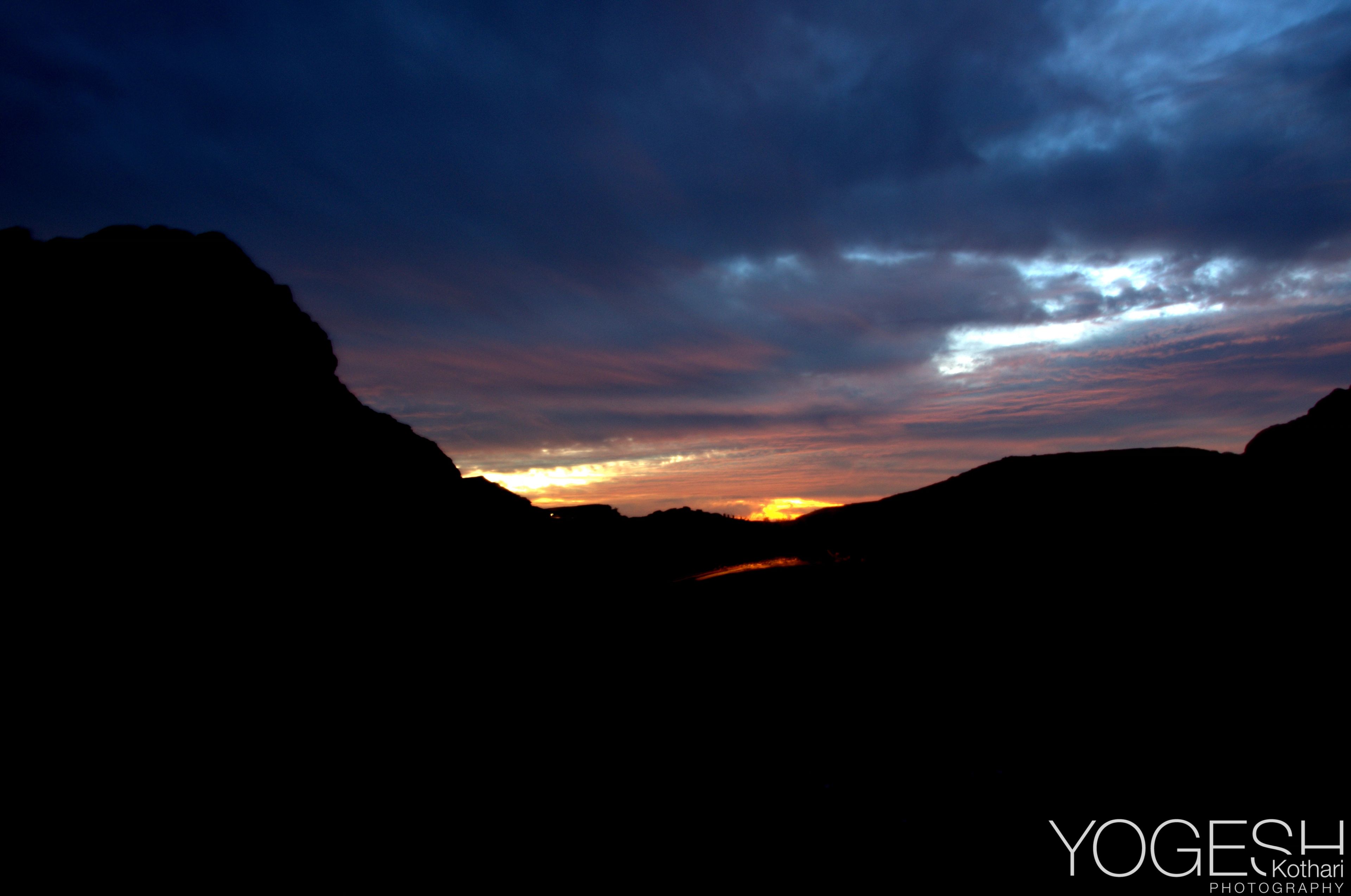 Dark mountain silhouettes beneath a thin band of orange sunset and blue cloud