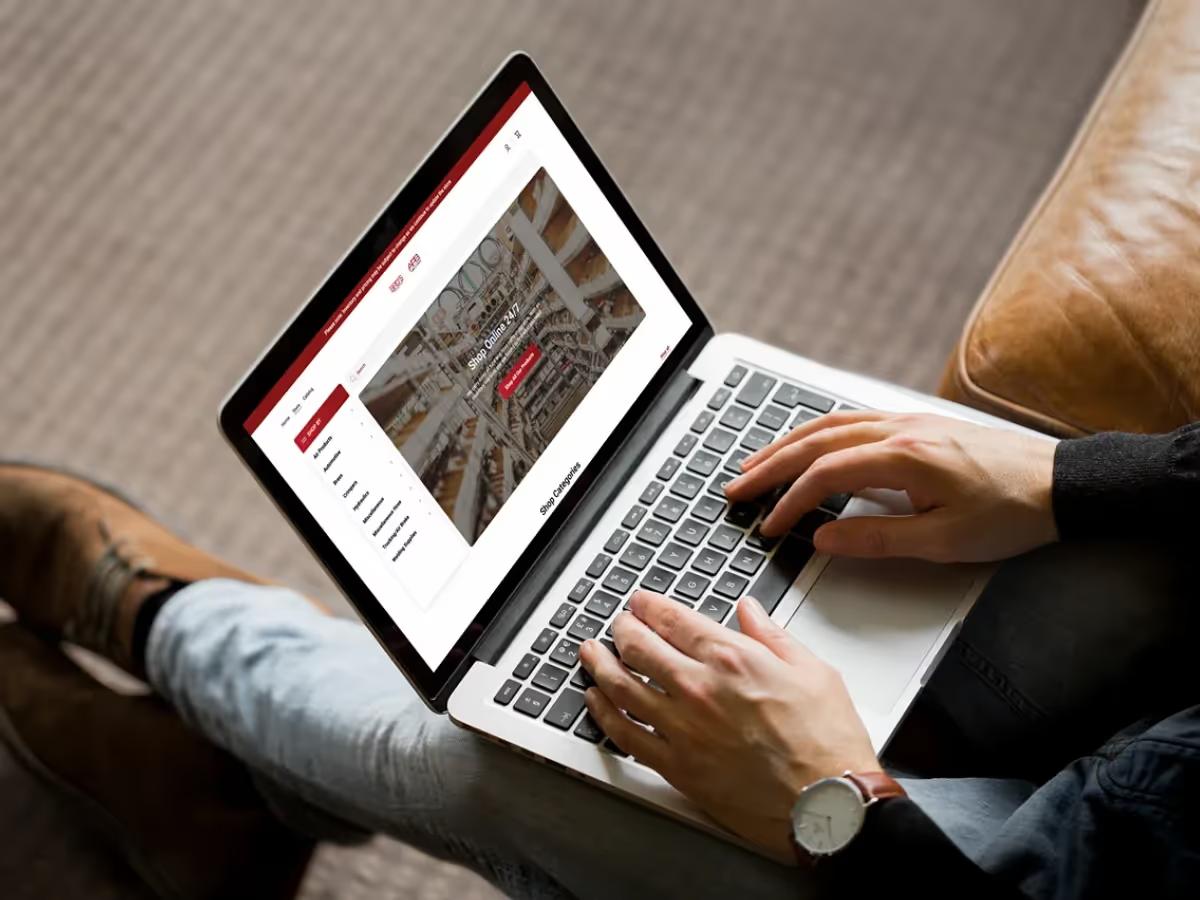 Laptop on a person's lap showing the Fluid Line Solutions Shopify store homepage with the Shop Online 24/7 banner and category menu