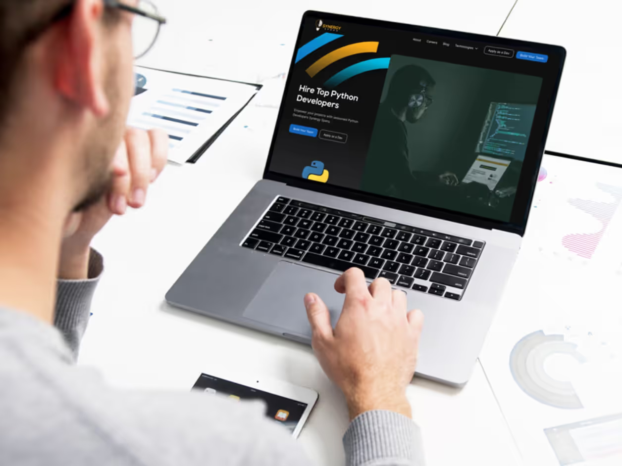 Man at desk browsing Synergy Sparq Hire Top Python Developers SEO page on MacBook with Python logo and developer image on dark background