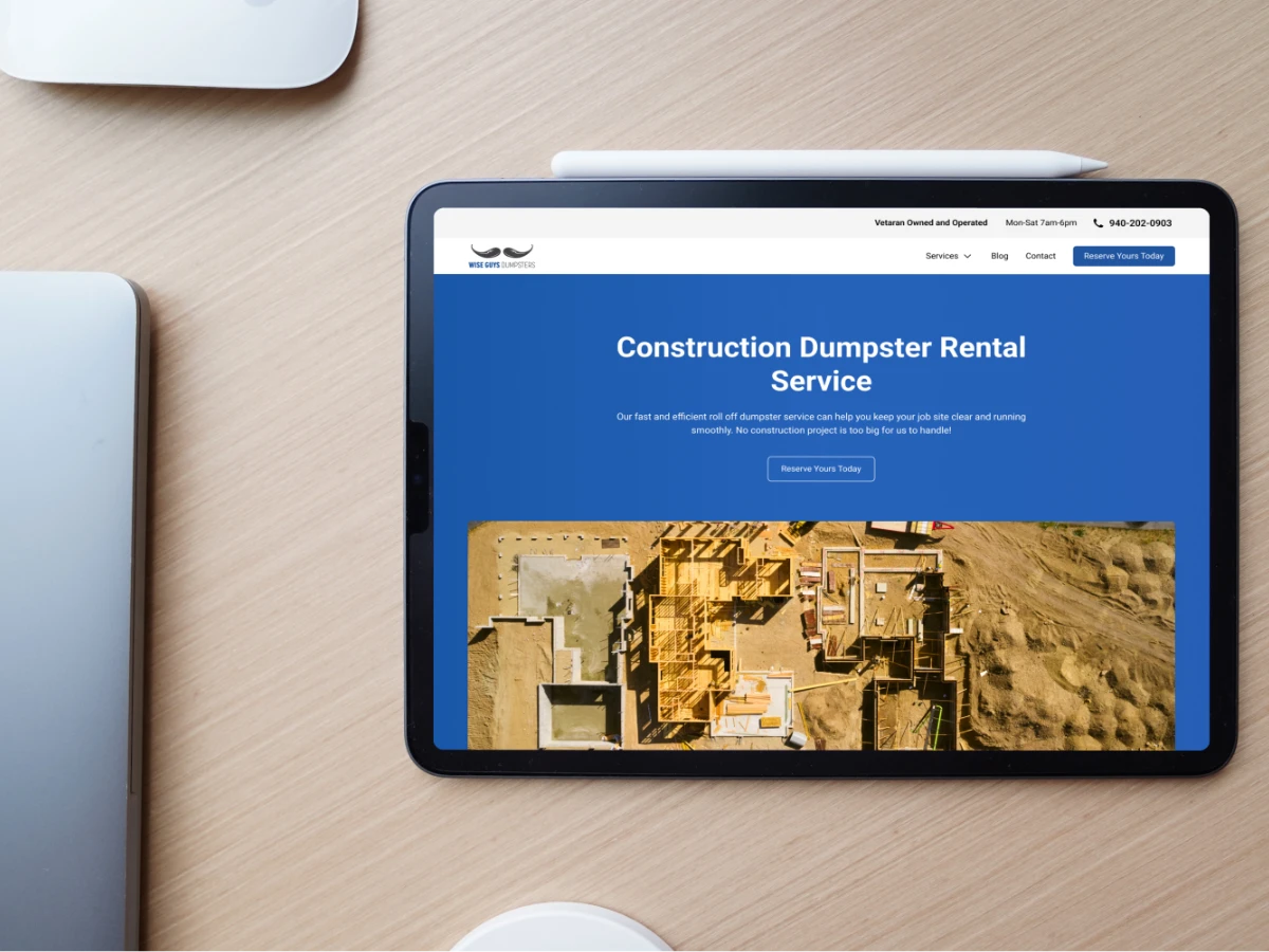 iPad on a wooden desk showing the Wise Guys Dumpsters Construction Dumpster Rental Service page with an aerial photo of a home under construction