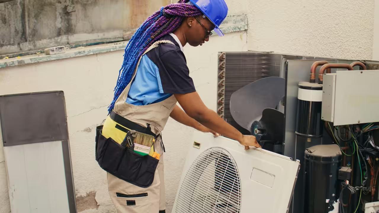 An HVAC technician working on an outdoor condenser unit, the urgent repair call that goes to whichever company answers the phone first.