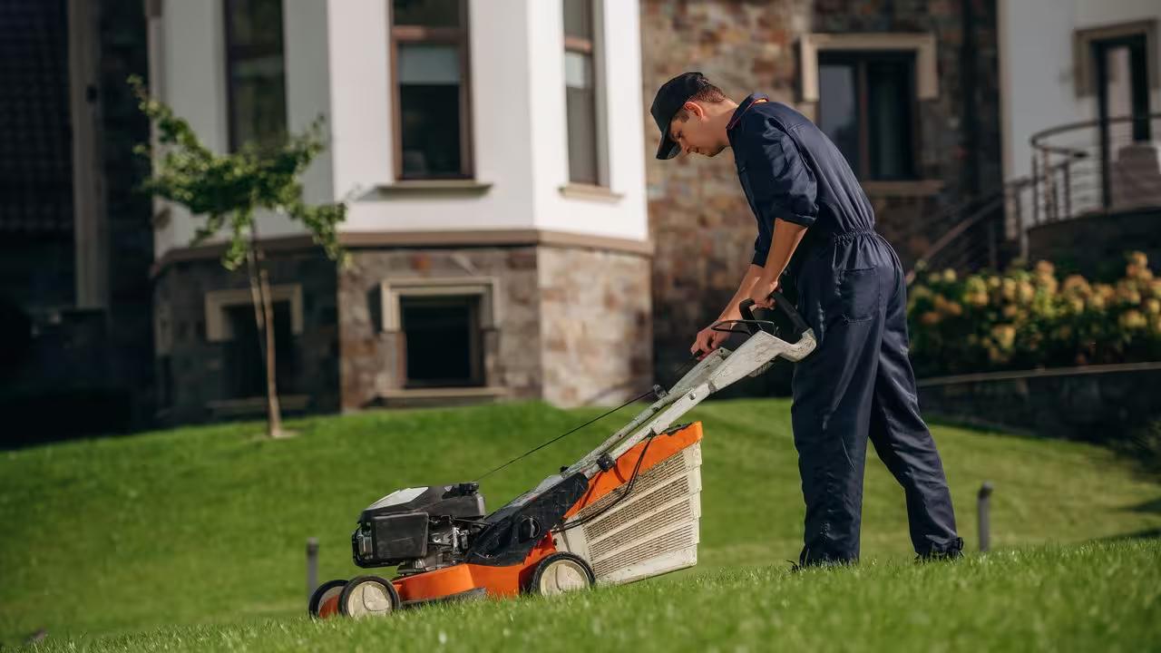 A lawn care professional mowing a residential front yard with the work truck at the curb, the route density that drives lawn care economics.