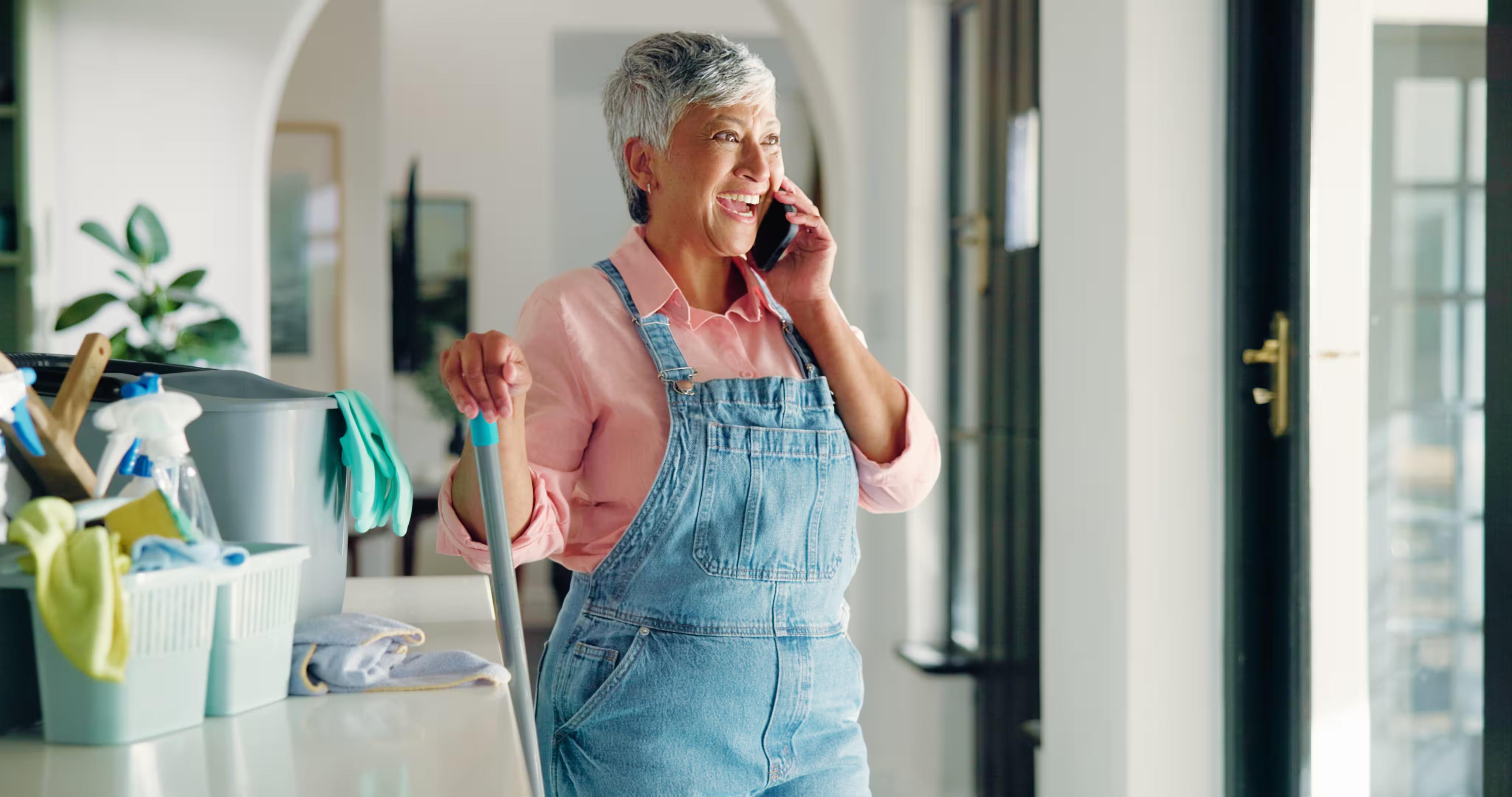A cleaner taking a phone call mid-job beside her caddy of supplies, answering a new lead inside the five minutes that decide whether it becomes a booking.