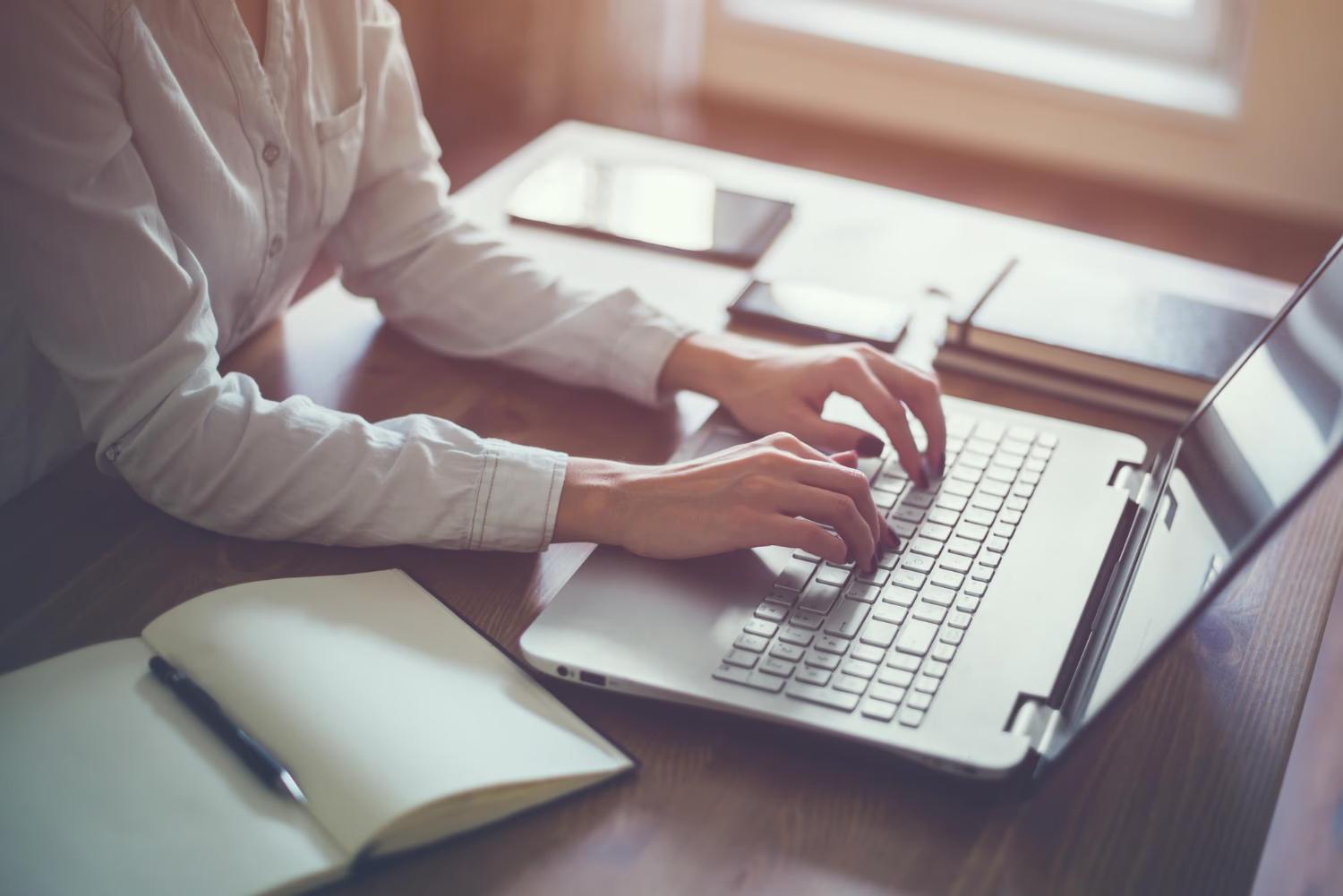 woman updating her keywords on her website on her laptop at a table with stuff on the table