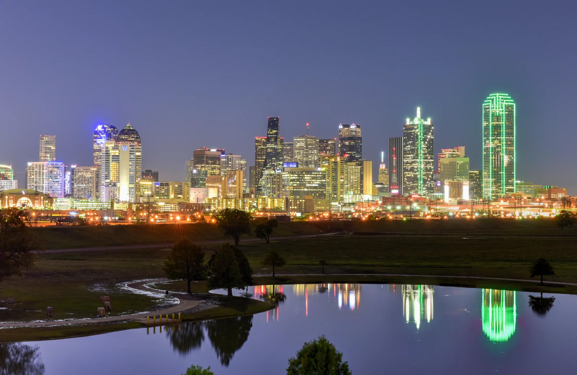 The Downtown Dallas skyline lit at night, reflected in the Trinity River