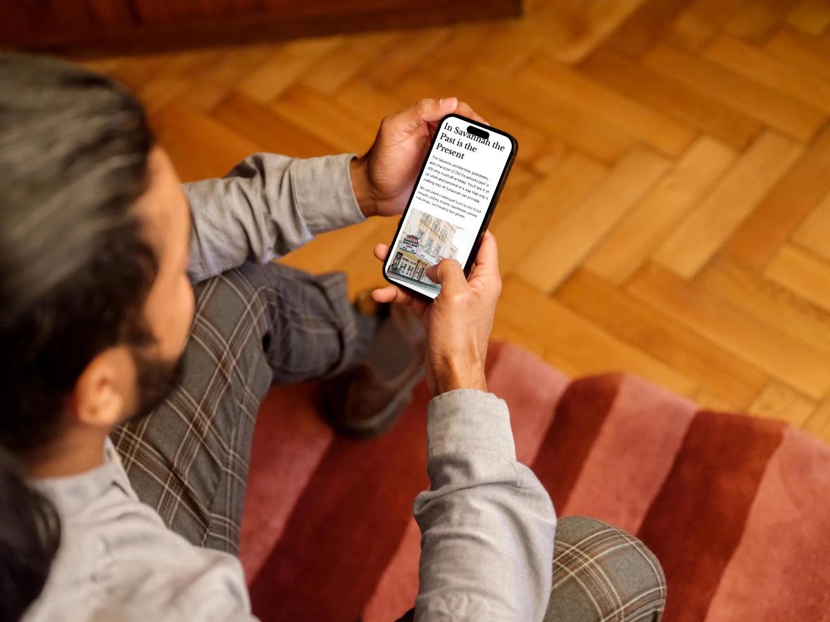Man holding a phone showing the Savannah Walks About page section In Savannah the Past is the Present with a photo of a historic downtown building